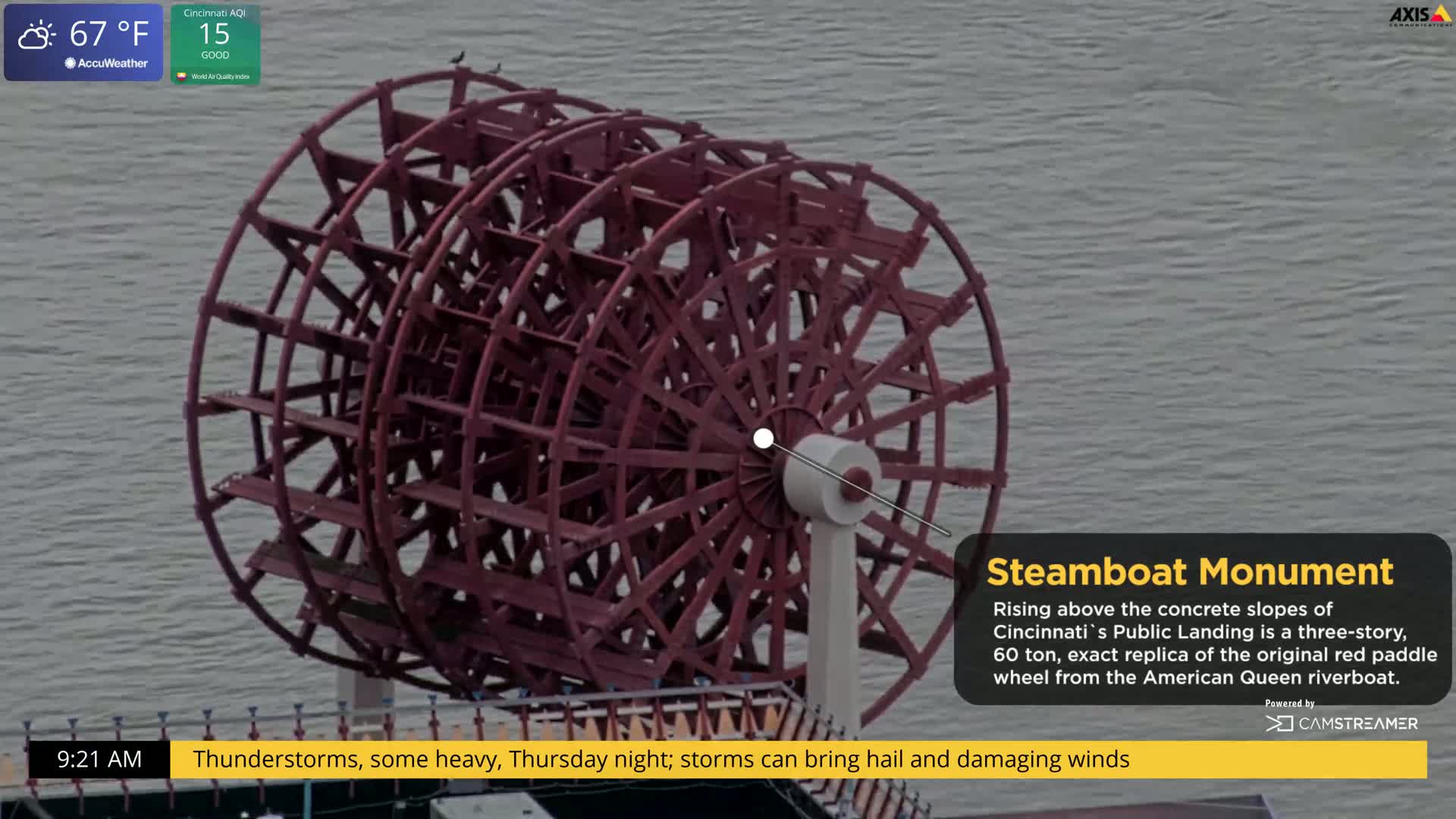 A large, red paddle wheel rises above a body of water under a partly cloudy sky, with thunderstorms predicted for the evening.