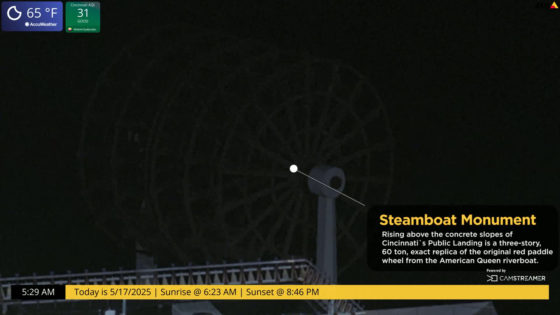 A large, dark-colored paddle wheel stands against a night sky.