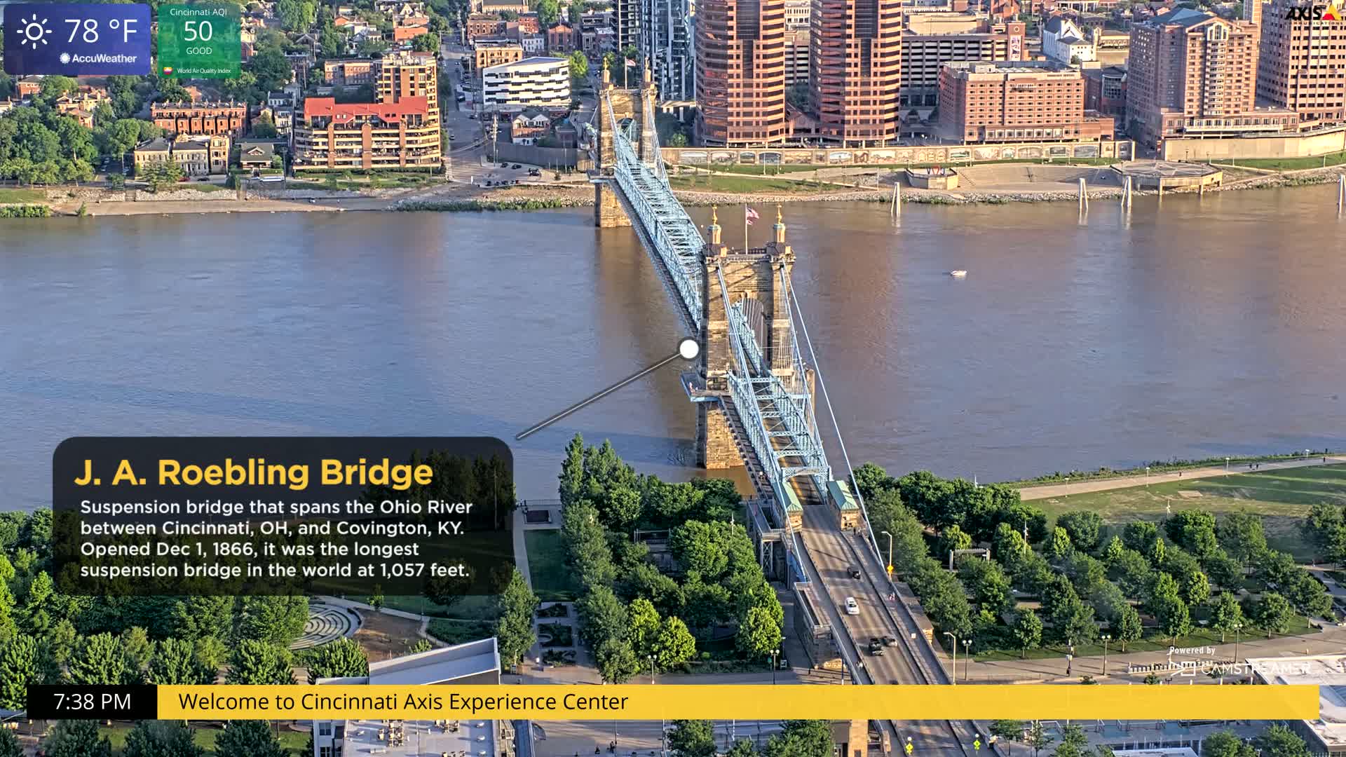 An aerial view shows a suspension bridge spanning a wide river on a partly sunny day with a temperature of 78°F.