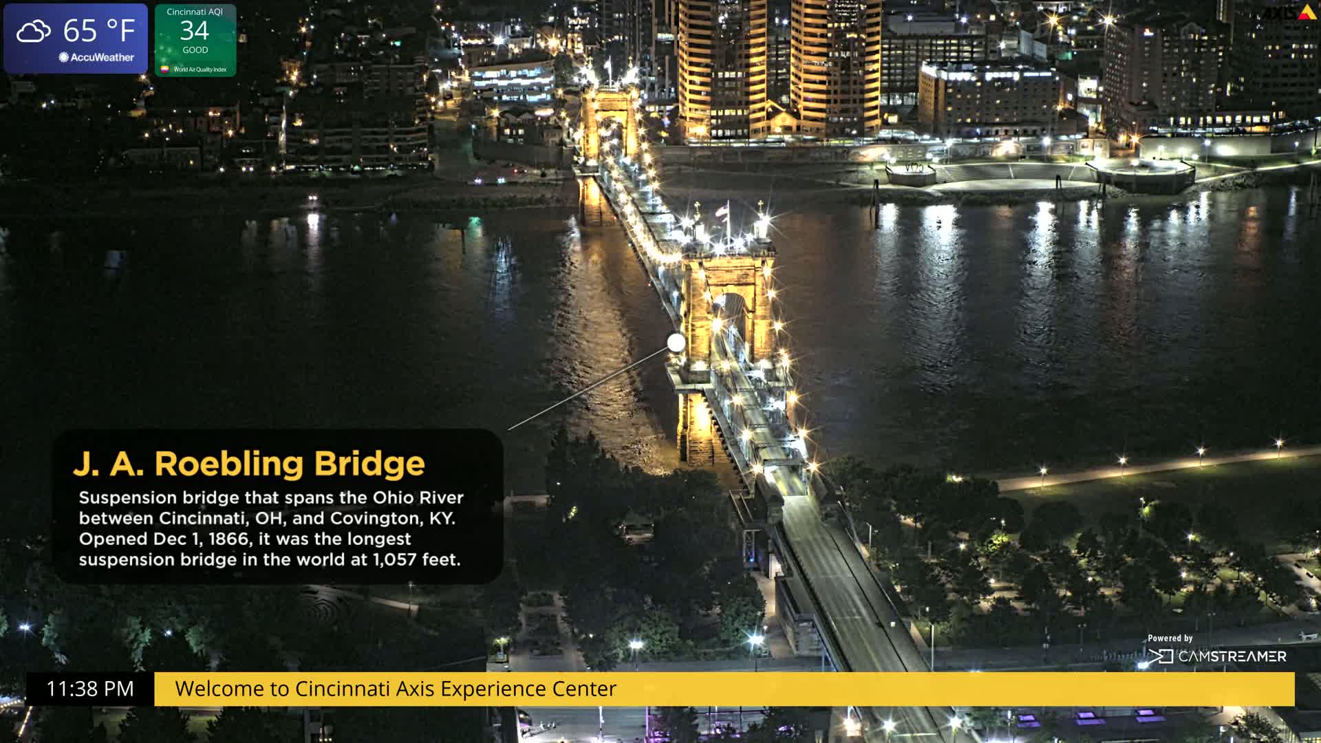 A lit suspension bridge spans a dark river at night under a clear sky.