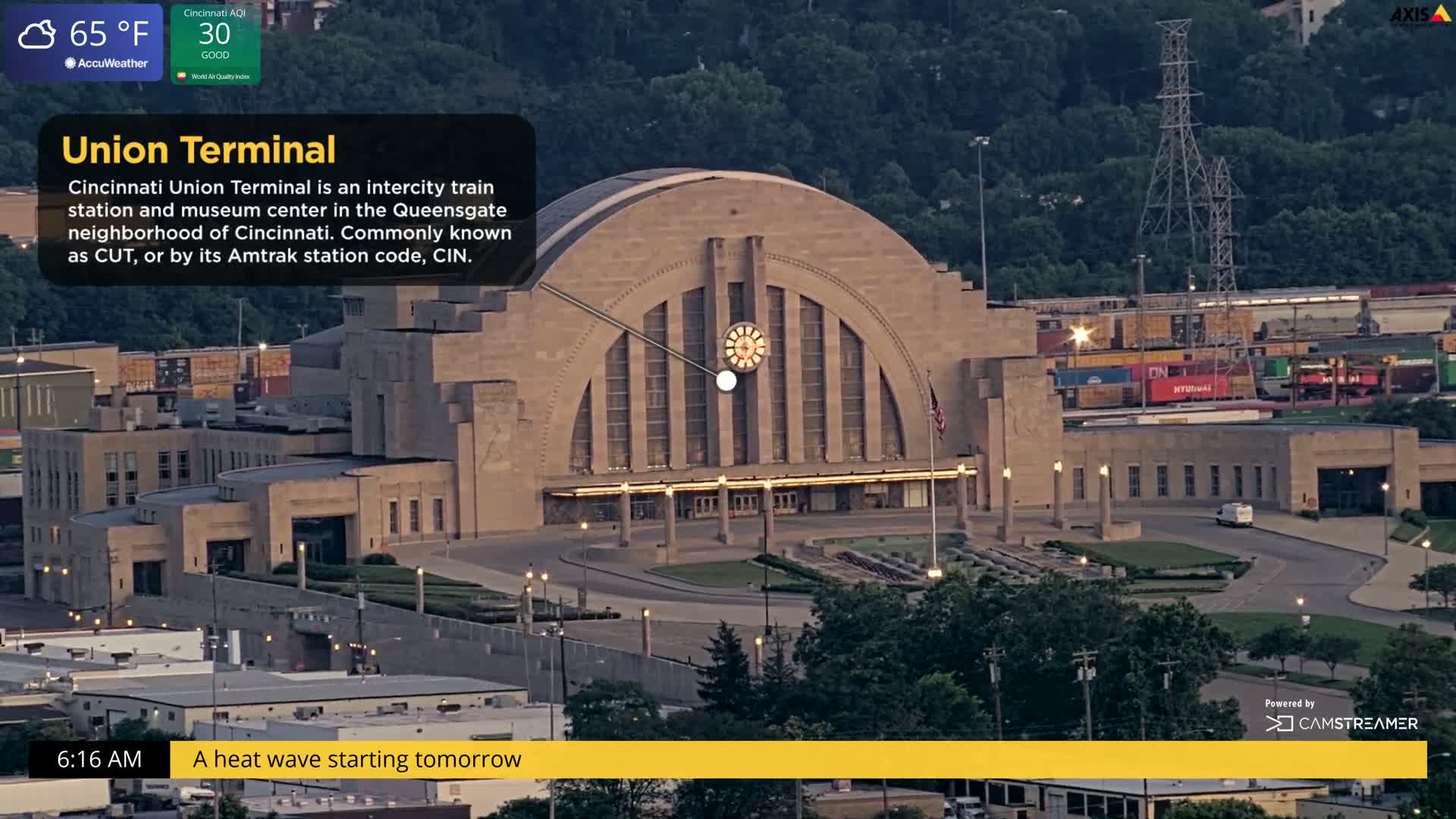 An aerial view of a large, tan train station at dusk, under partly cloudy skies and a temperature of 65°F.