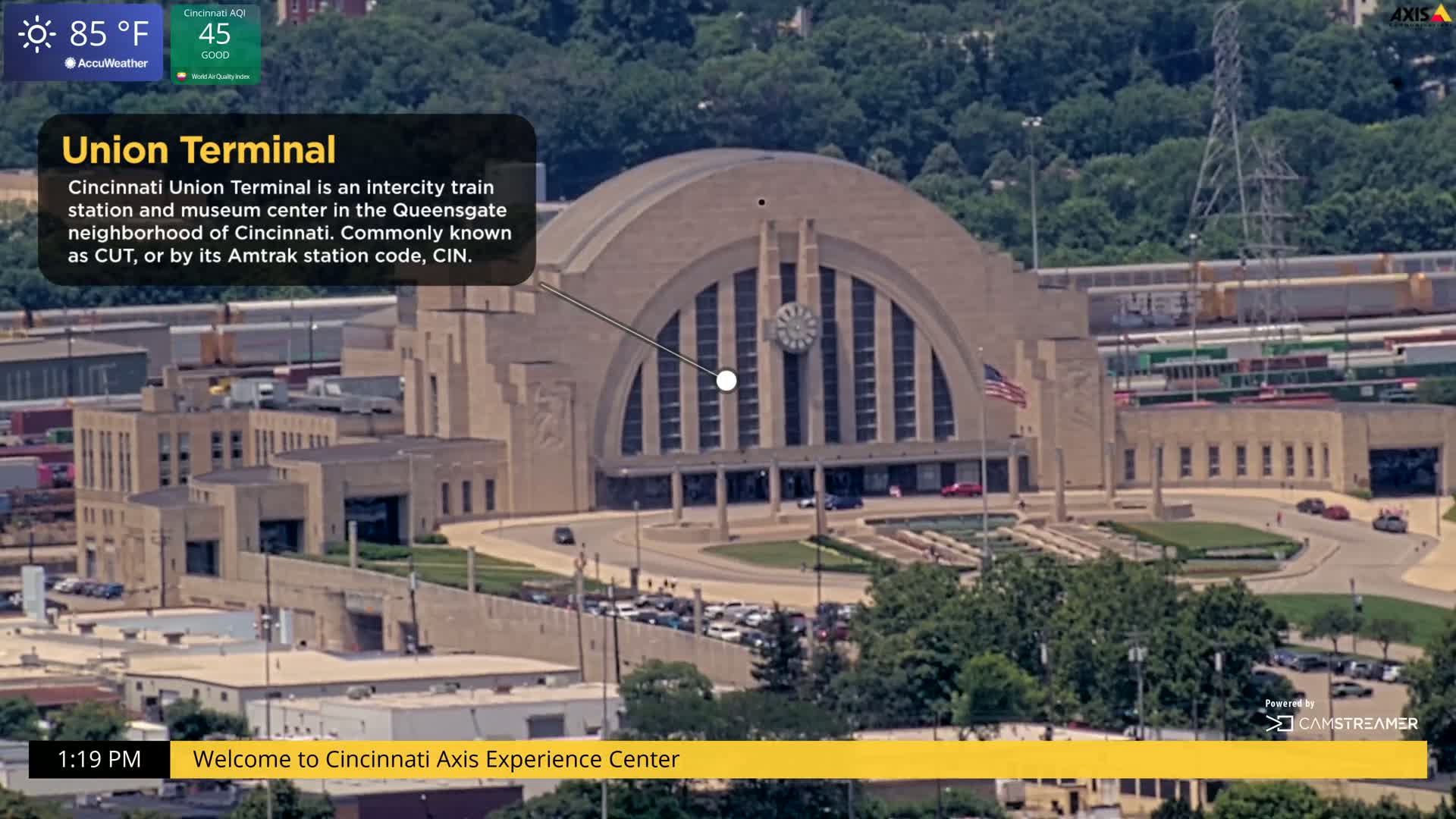 An aerial view shows a large, curved train station on a sunny day.