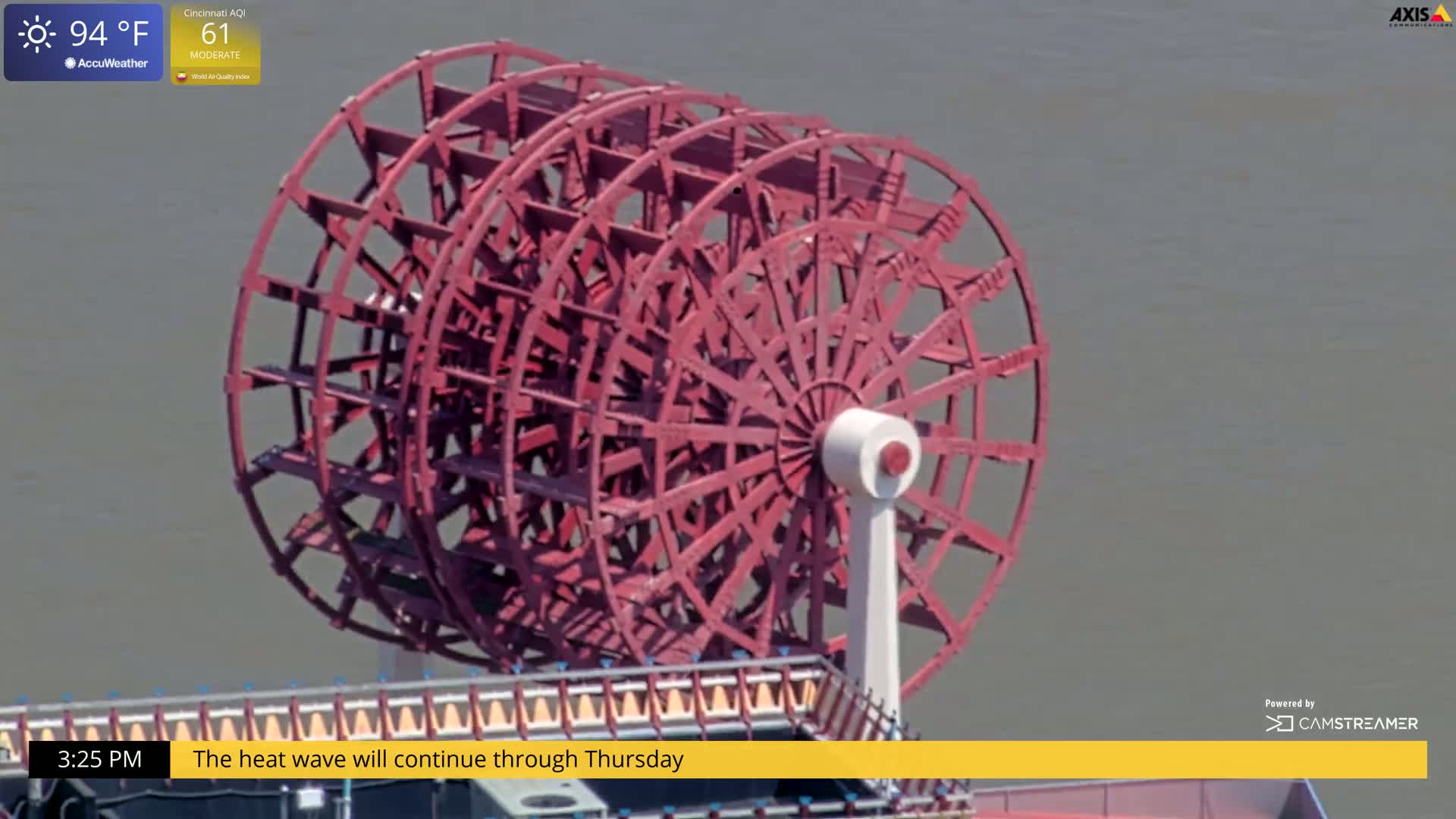 A large, reddish-brown paddle wheel is visible on a boat on a calm, gray body of water on a sunny, 94°F day.