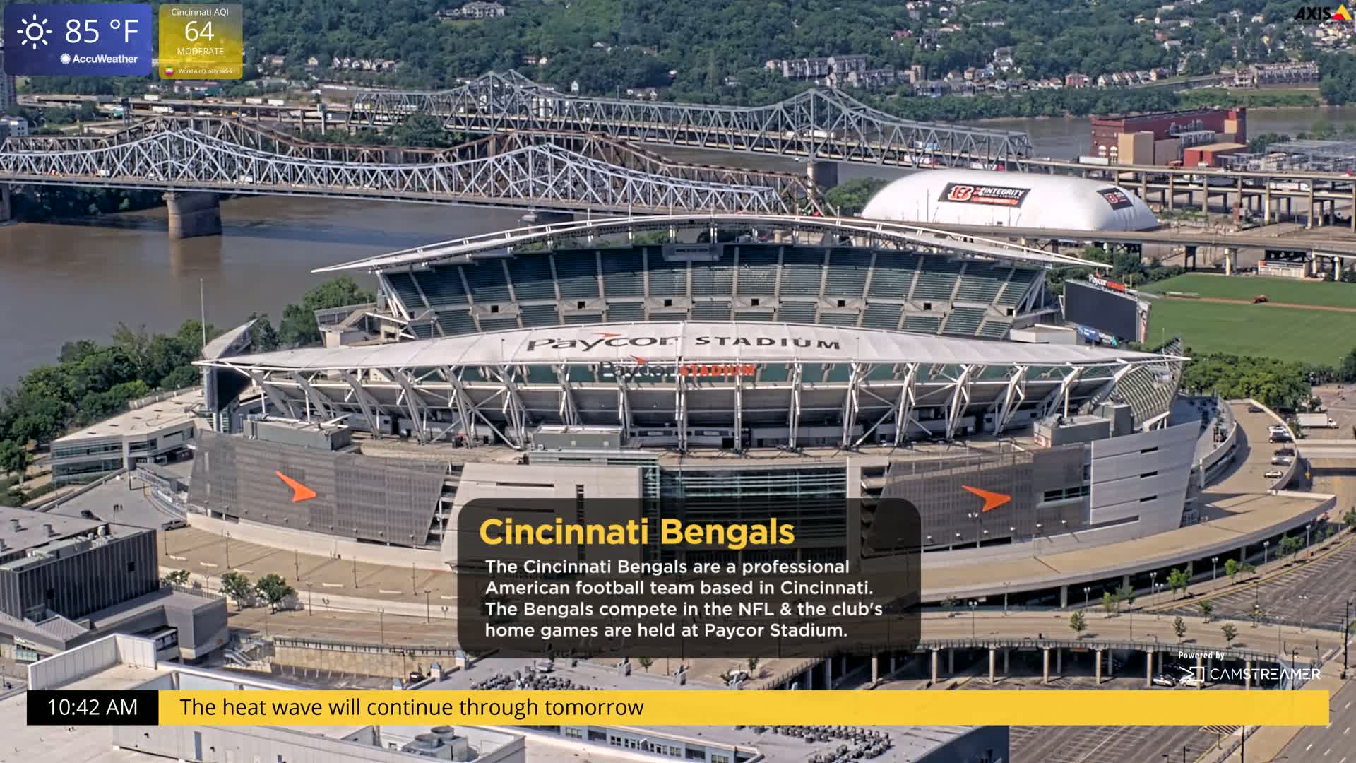 A wide aerial view shows Paycor Stadium on a sunny, hot day, with a river and bridge in the background.
