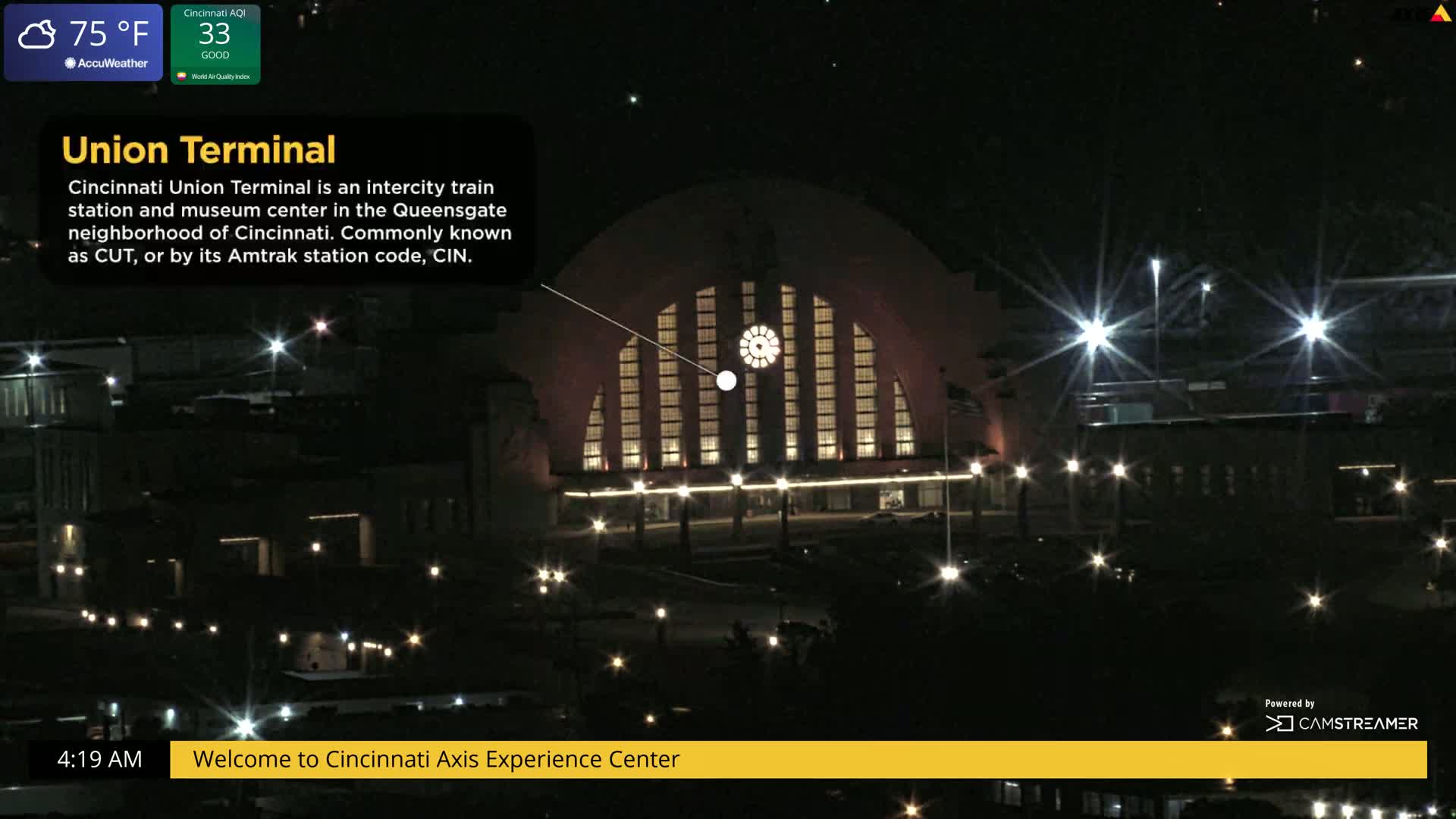 A nighttime, illuminated view of a large, arched train station.