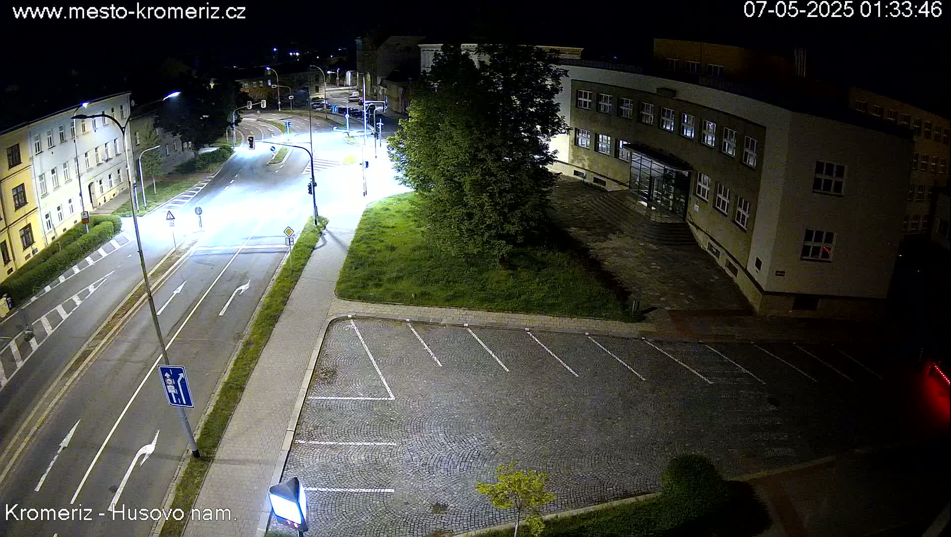 A nighttime, overhead view of a street intersection with an empty parking lot and a multi-story building.