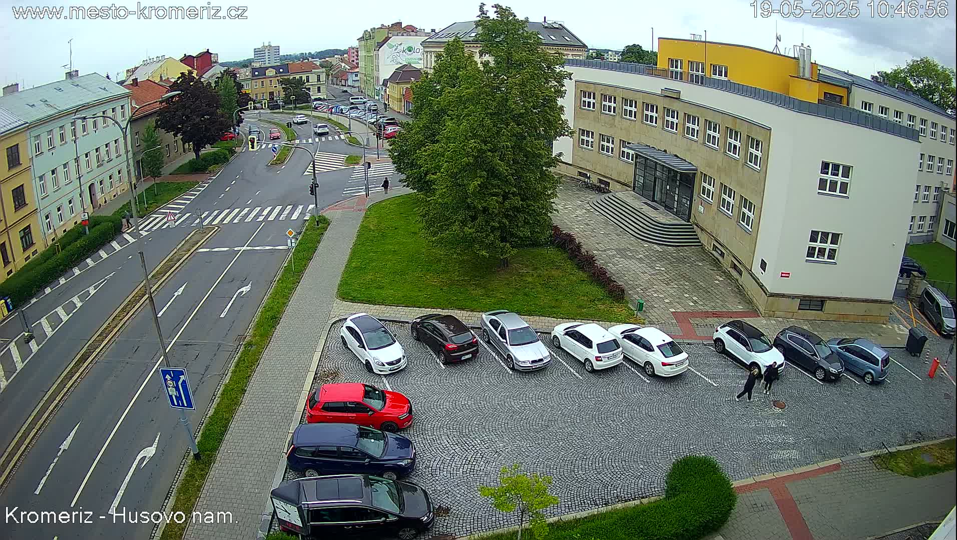 An overcast day reveals a city street scene with a parking lot containing several cars,  a large building, and a pedestrian crossing.