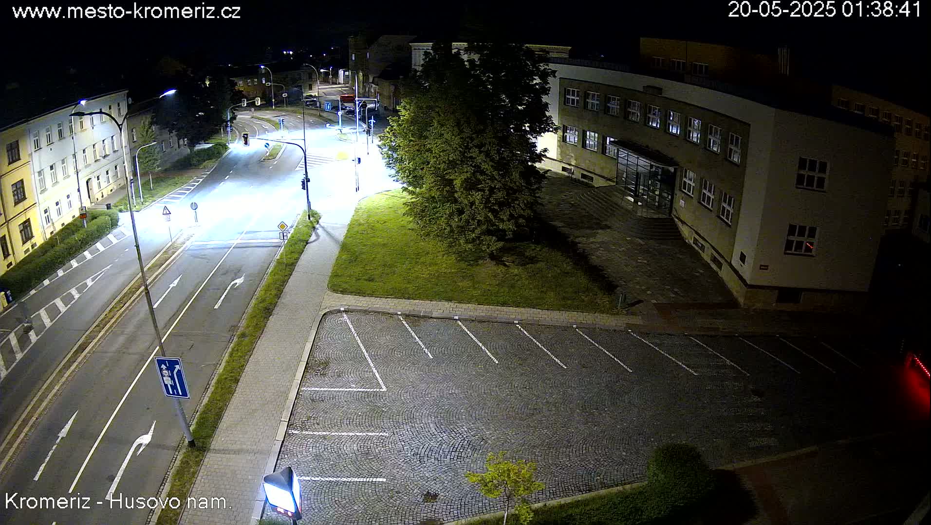 An empty cobblestone parking lot is adjacent to a quiet, dimly lit street at night.