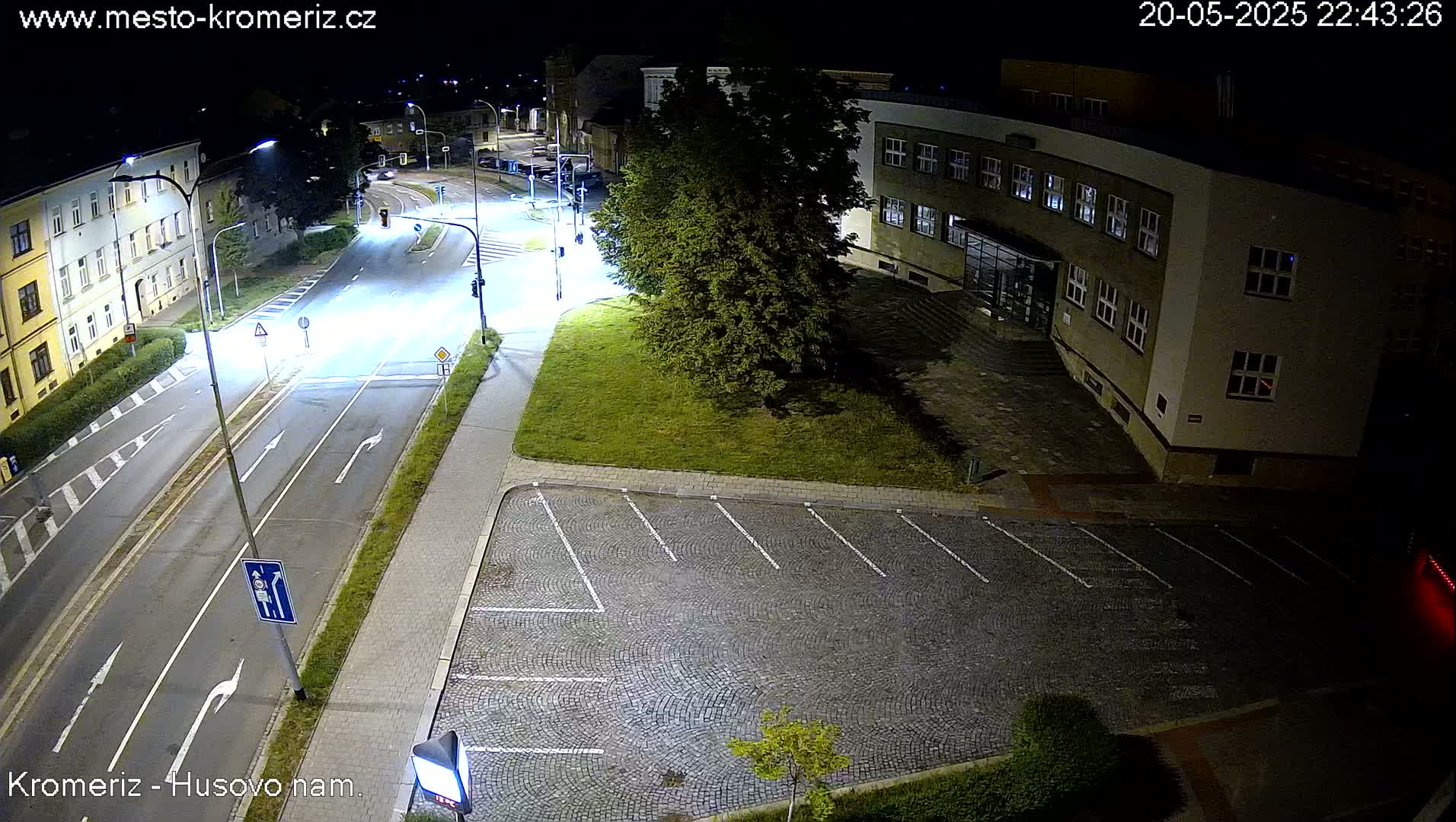 A nighttime view of a street intersection and empty parking lot next to a building, illuminated by streetlights.