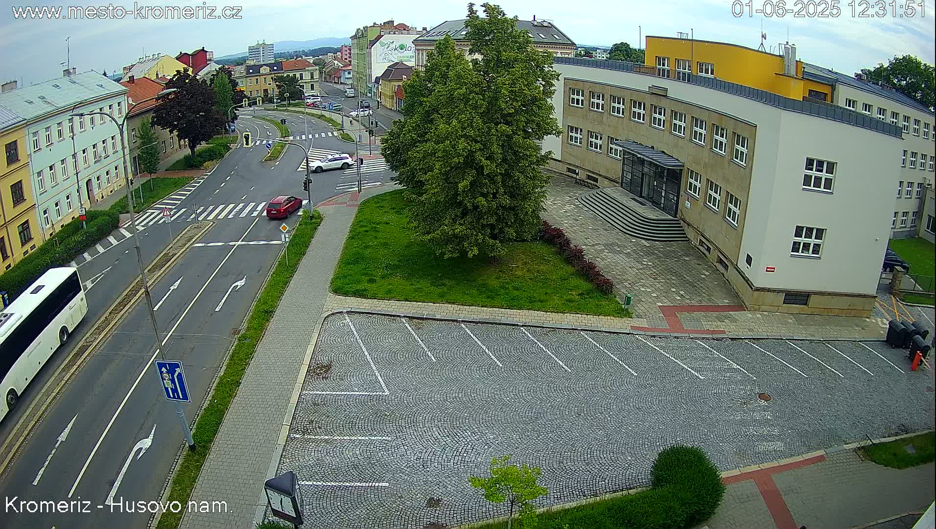 A mostly empty cobblestone parking lot is adjacent to a street intersection and a large building under a partly cloudy sky.