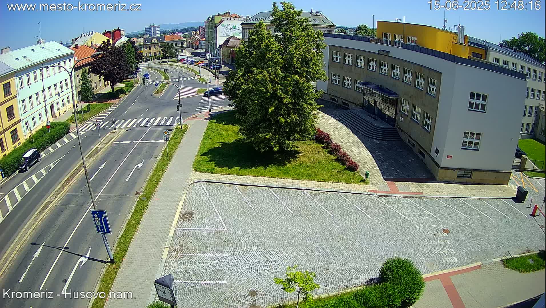 A sunny day view of a city intersection with a large building and an empty cobblestone parking lot.