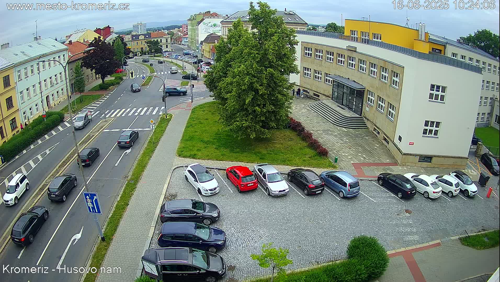 A street scene on an overcast day shows cars parked in a lot next to a building, with other cars driving on a road.