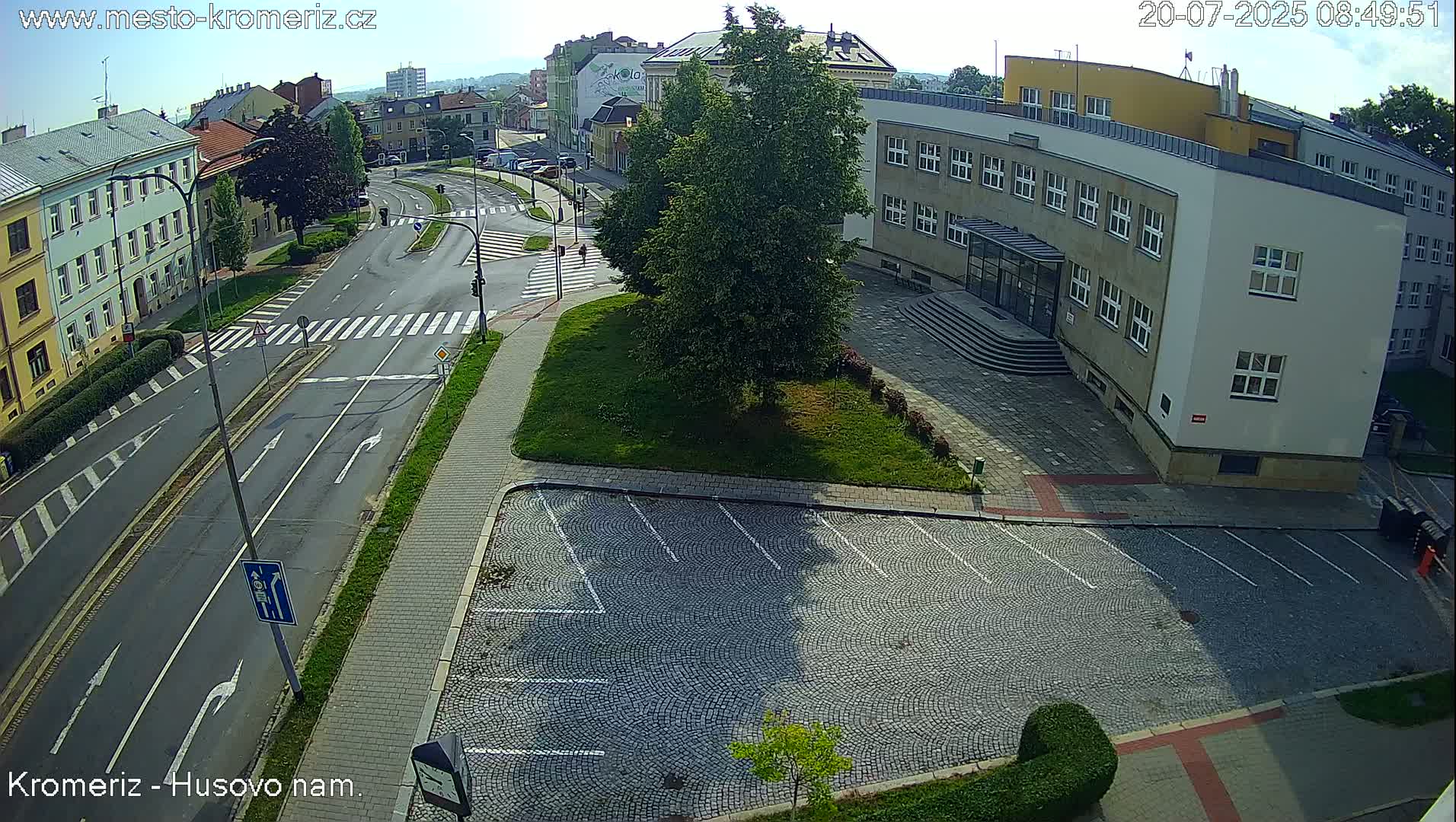 A sunny day reveals a paved parking lot next to a multi-story building and a street intersection with crosswalks and light poles.