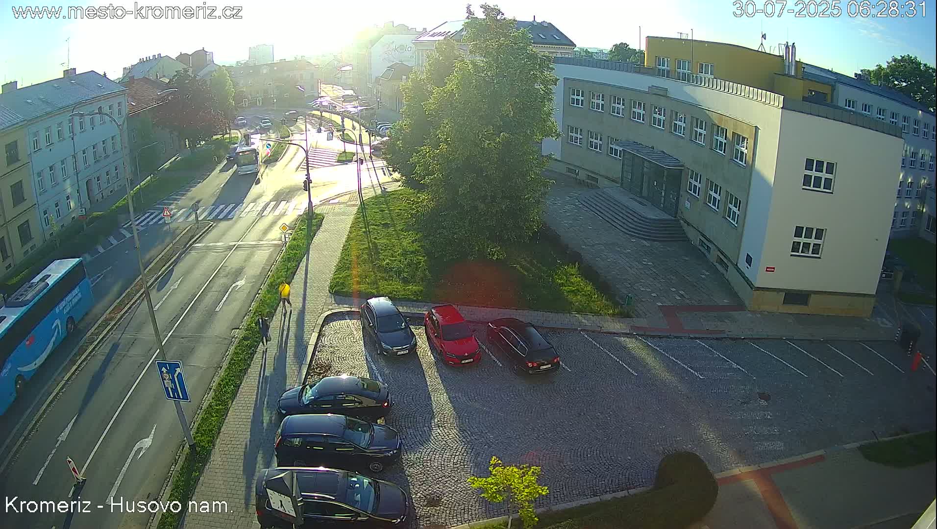 A sunny day reveals a paved parking lot next to a multi-story building and a street intersection with crosswalks and light poles.