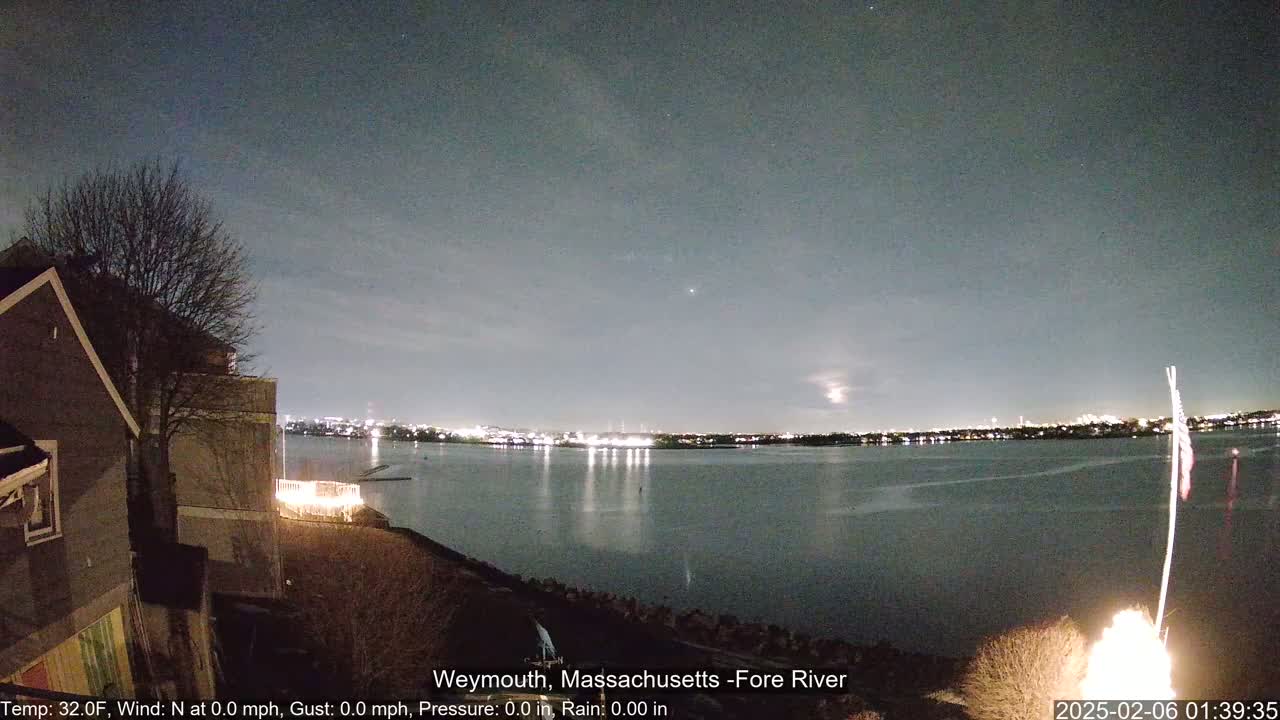 A nighttime view of a calm river reflecting city lights under a clear, dark sky.