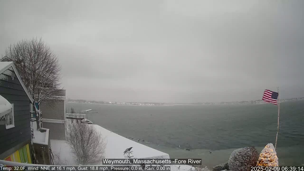 A snow-covered landscape overlooks a choppy body of water under a gray, overcast sky.