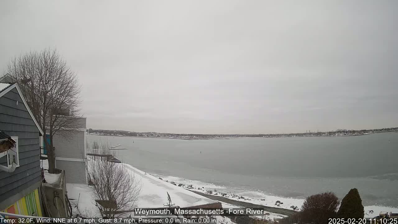 A snow-covered waterfront scene shows a partially frozen river under an overcast sky.