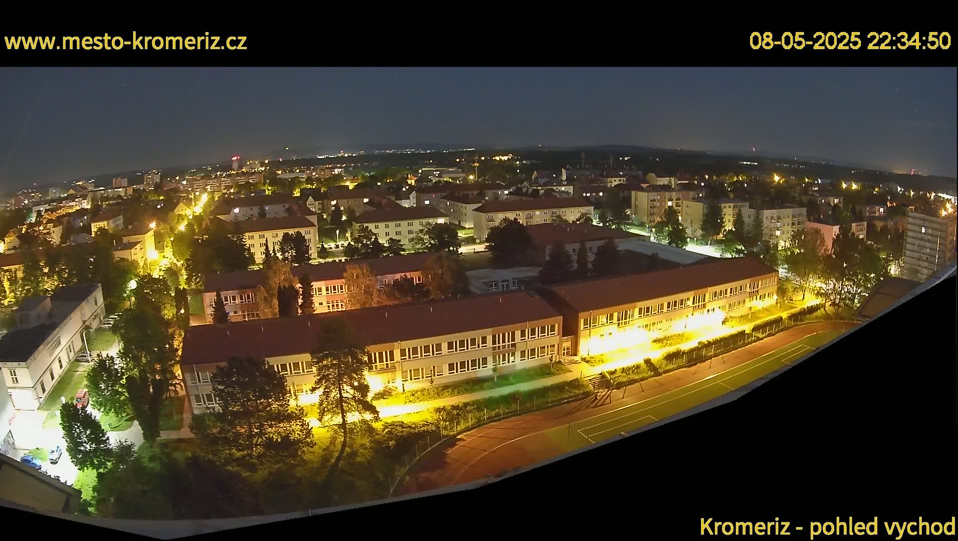 A nighttime aerial view shows a residential area with illuminated buildings, streets, and a running track.