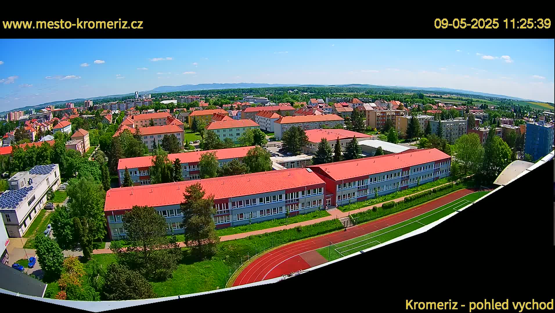 An aerial view shows a school complex with red roofs and a running track on a sunny day.