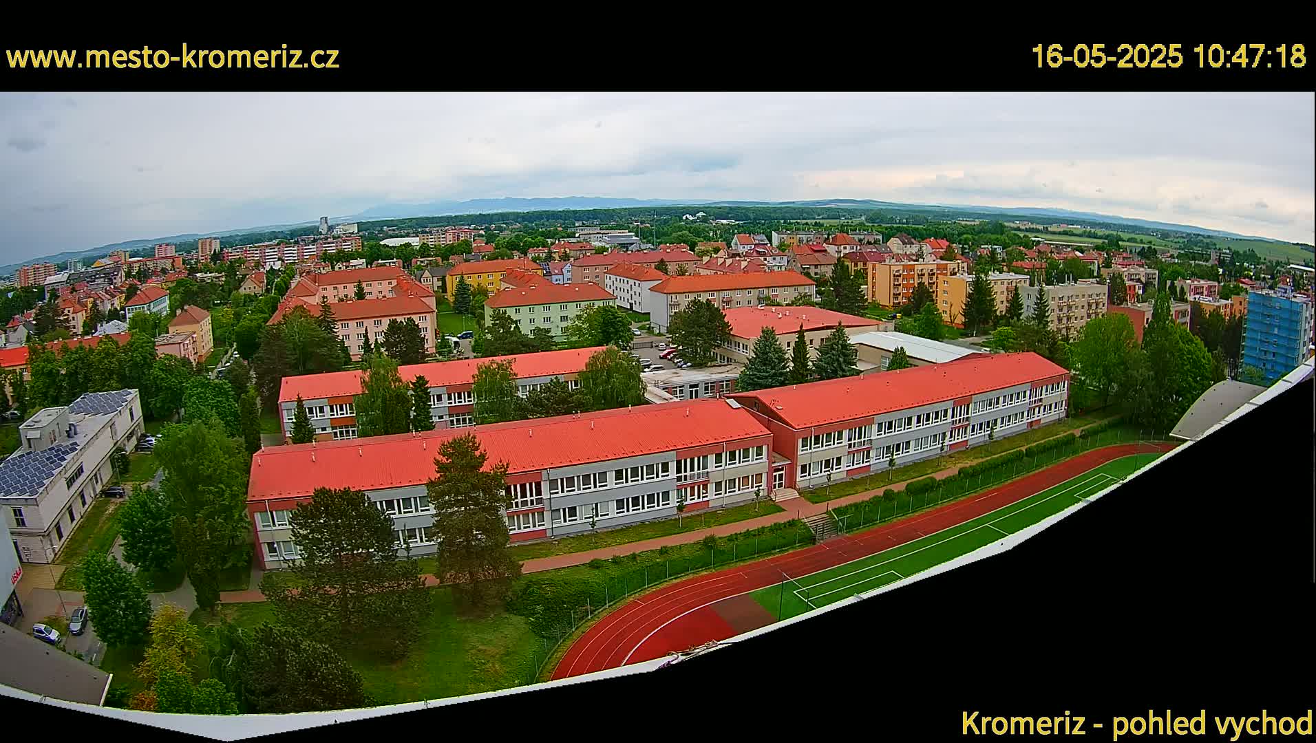 An aerial view of a town under an overcast sky shows a large school with red roofs and a running track next to a soccer field.