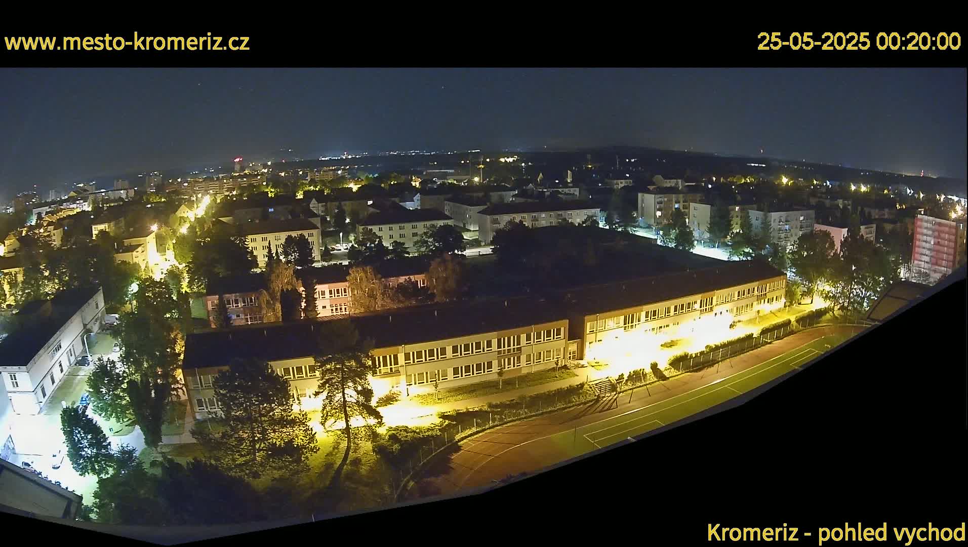 A nighttime, high-angle view of a residential area with illuminated buildings and a sports field.
