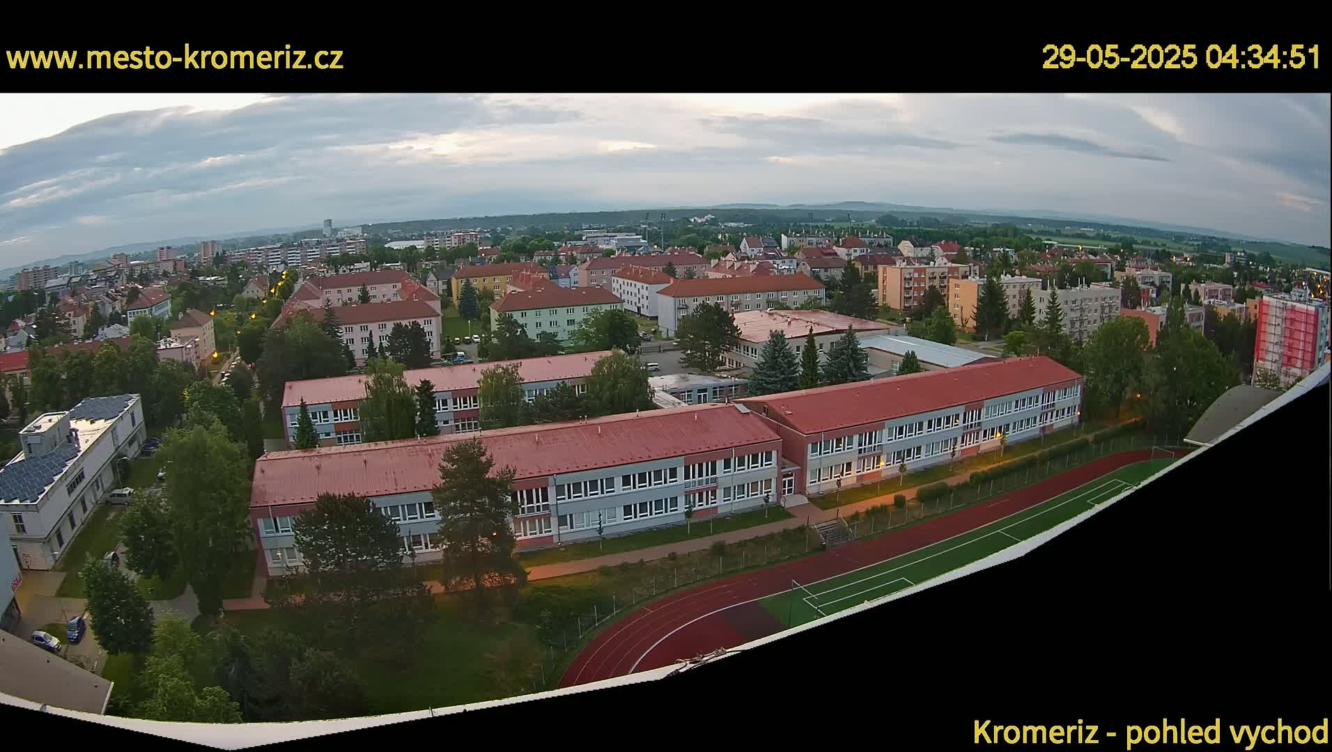 An aerial view of a residential area with several buildings and a running track, under a partly cloudy sky.