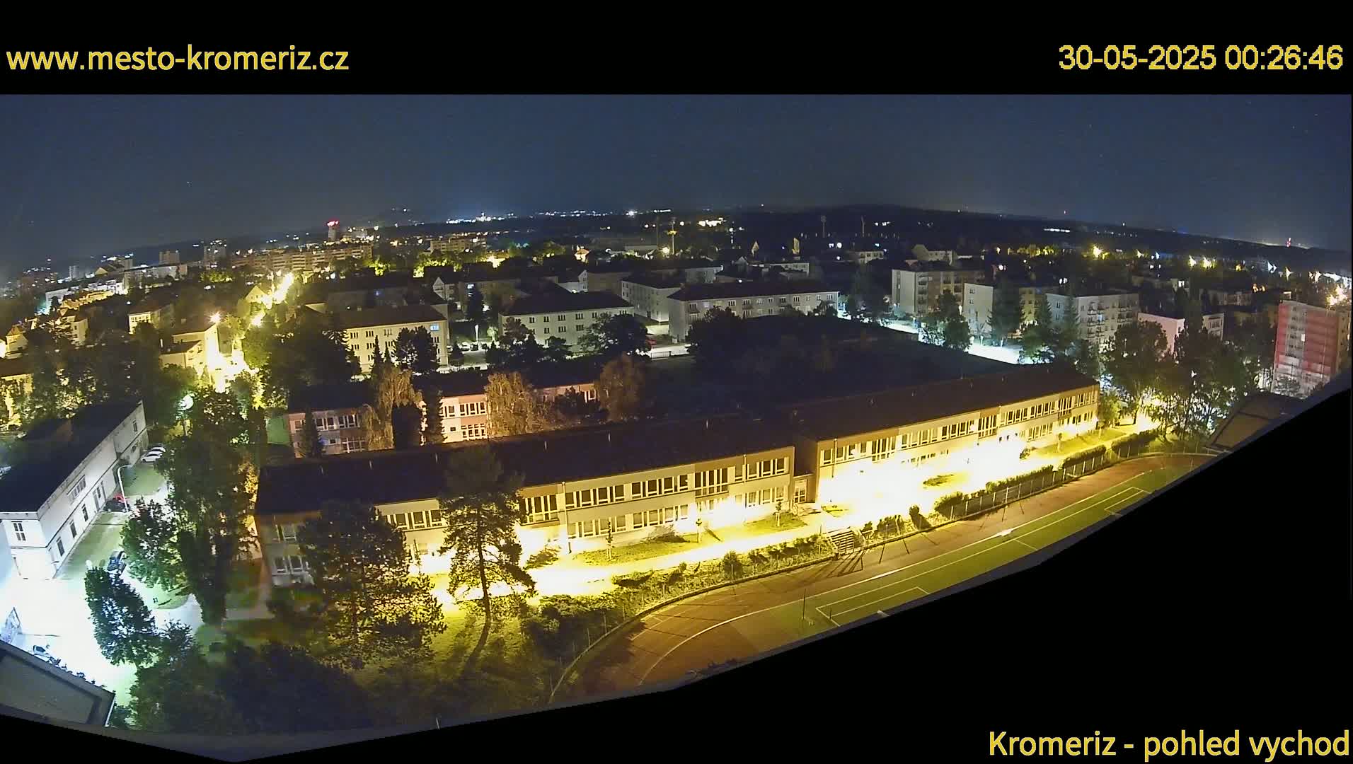 A nighttime aerial view of a residential area with illuminated buildings and a sports field.
