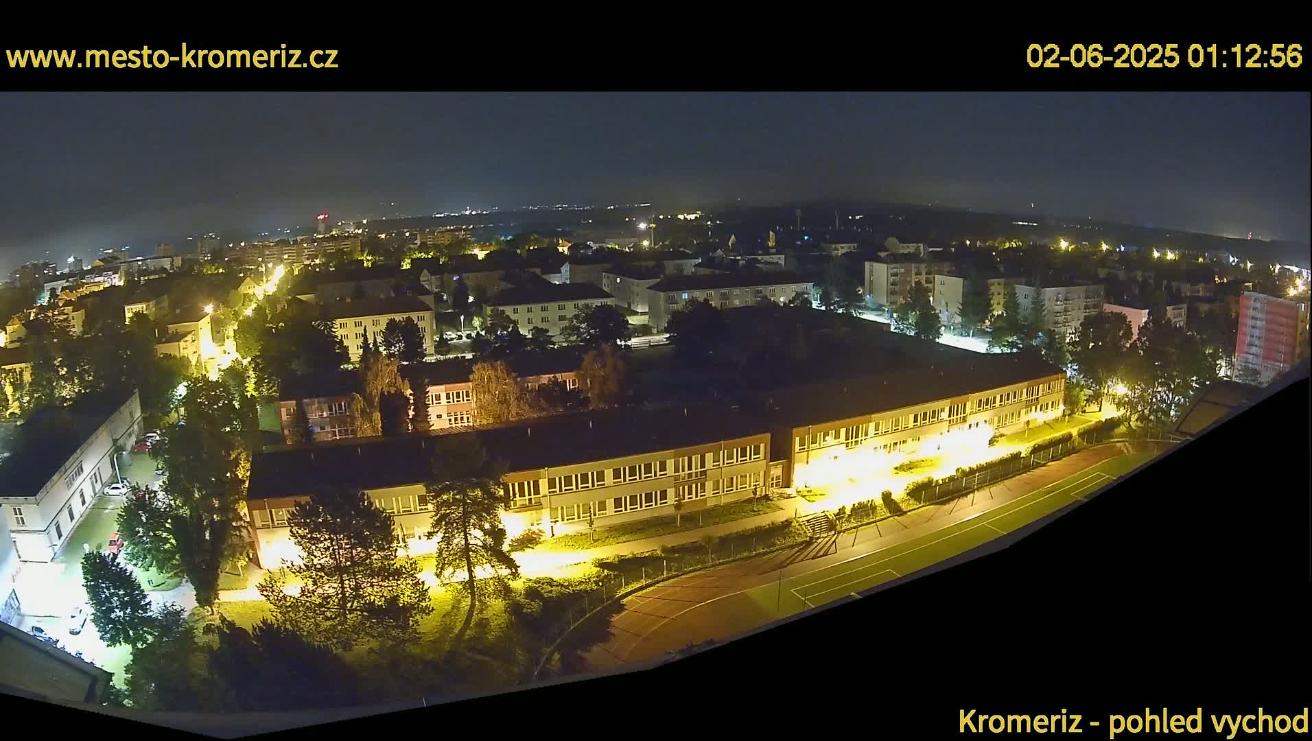 A nighttime aerial view shows a town's illuminated buildings and a sports field.
