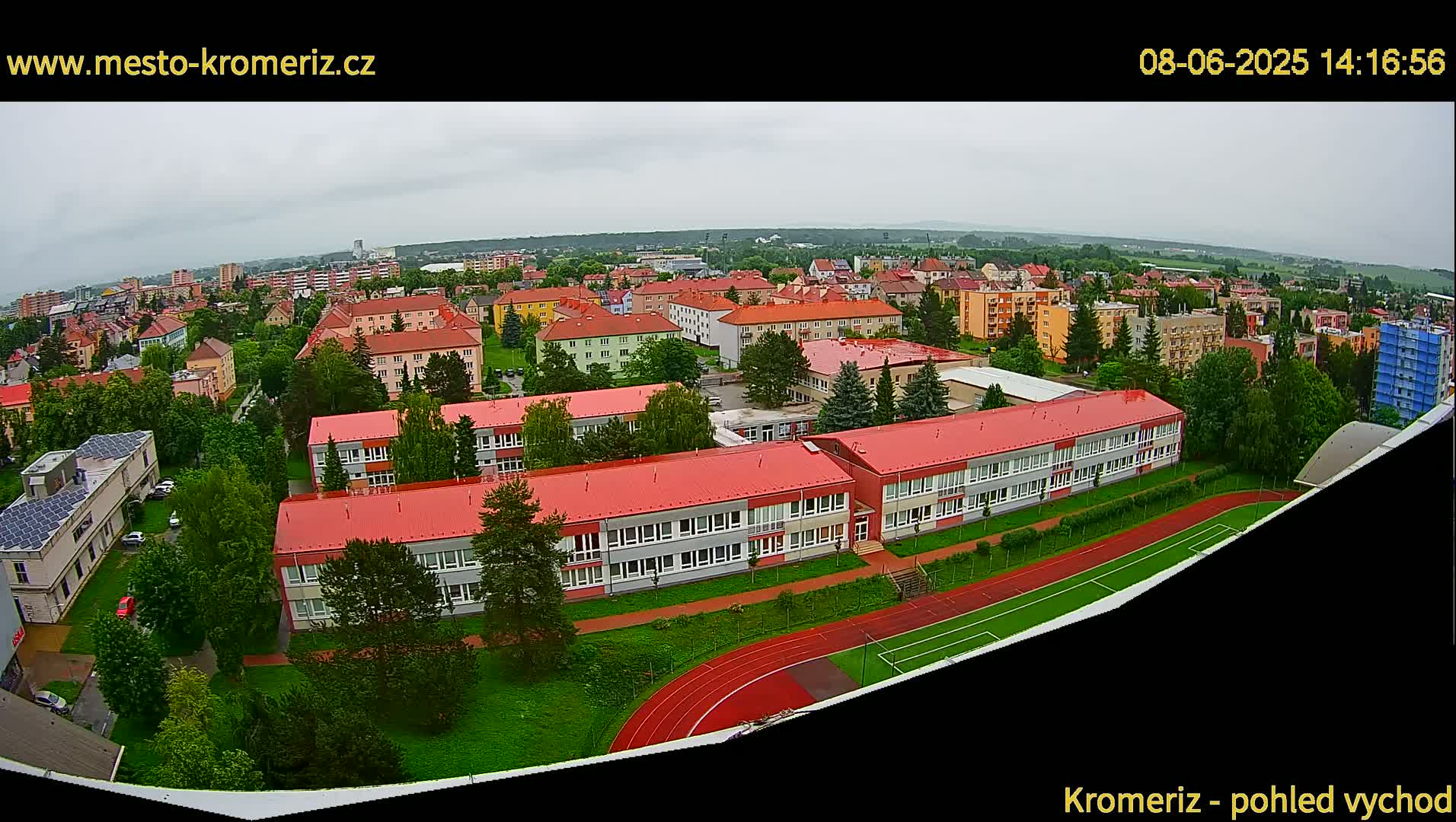 An aerial view shows a large school with red roofs and a running track on an overcast day.