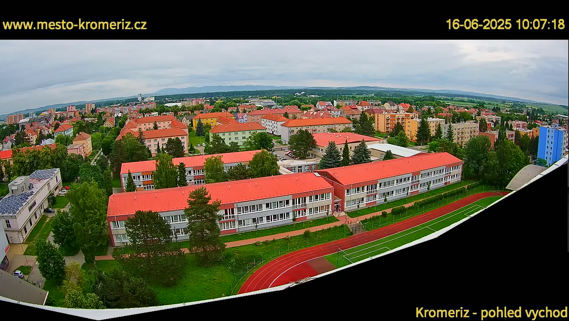 An aerial view of a town under a cloudy sky shows several buildings, including a large school with a red roof and a running track.