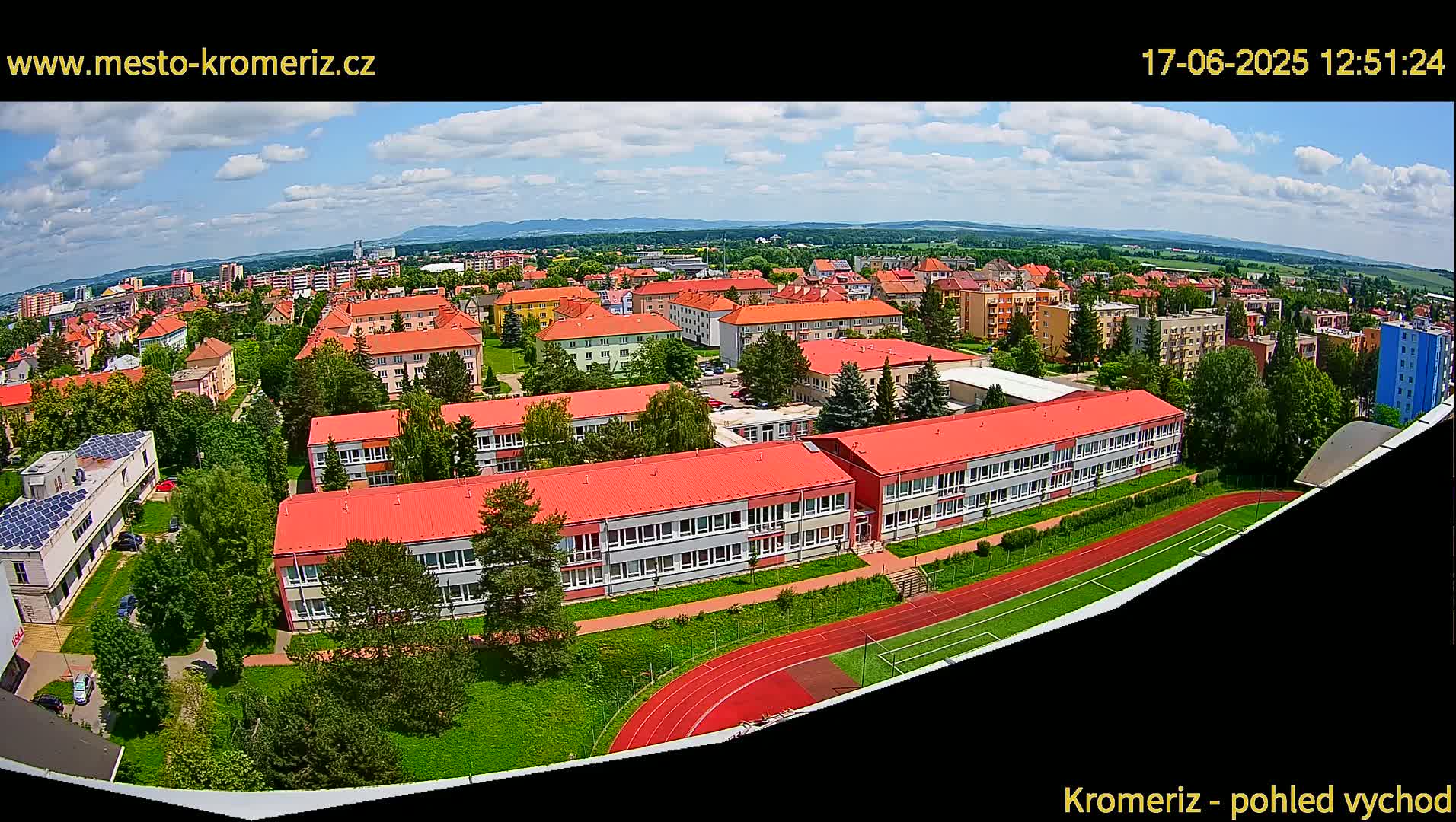 A partly cloudy day reveals a sprawling residential area with numerous low-rise buildings and a large school complex featuring a running track.
