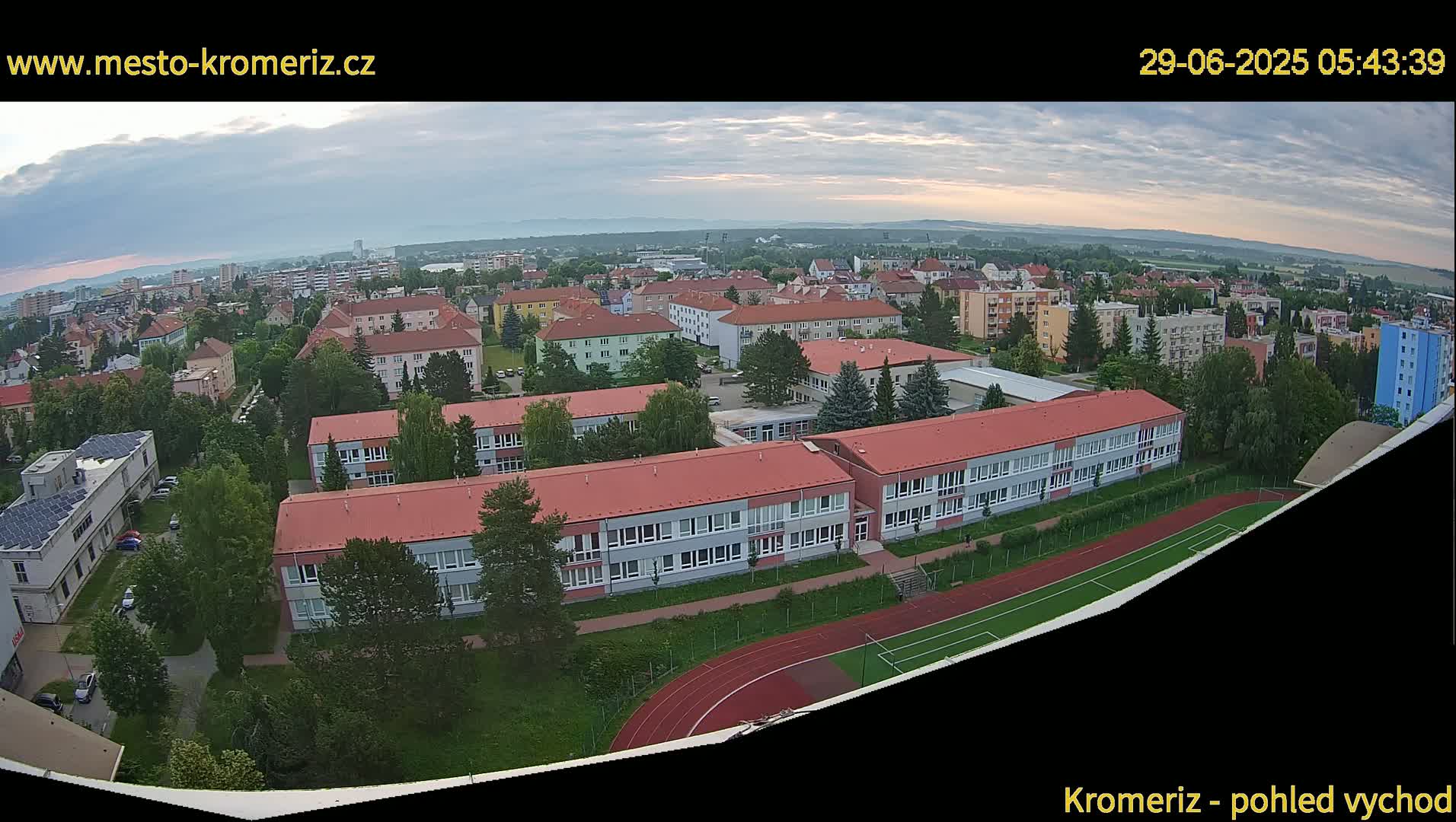 An aerial view shows a school with red roofs and a running track on a partly cloudy morning.