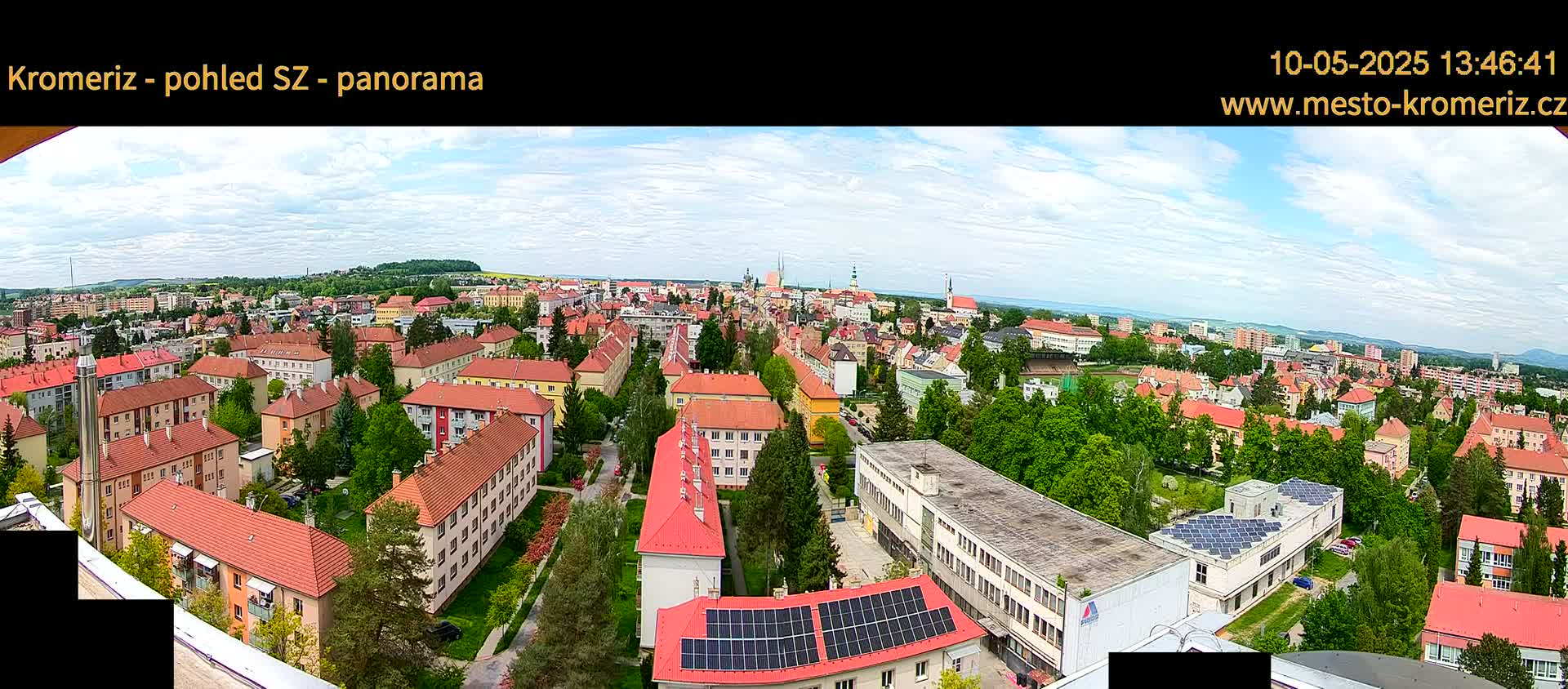 A panoramic view of a town with predominantly red-roofed buildings under a partly cloudy sky.