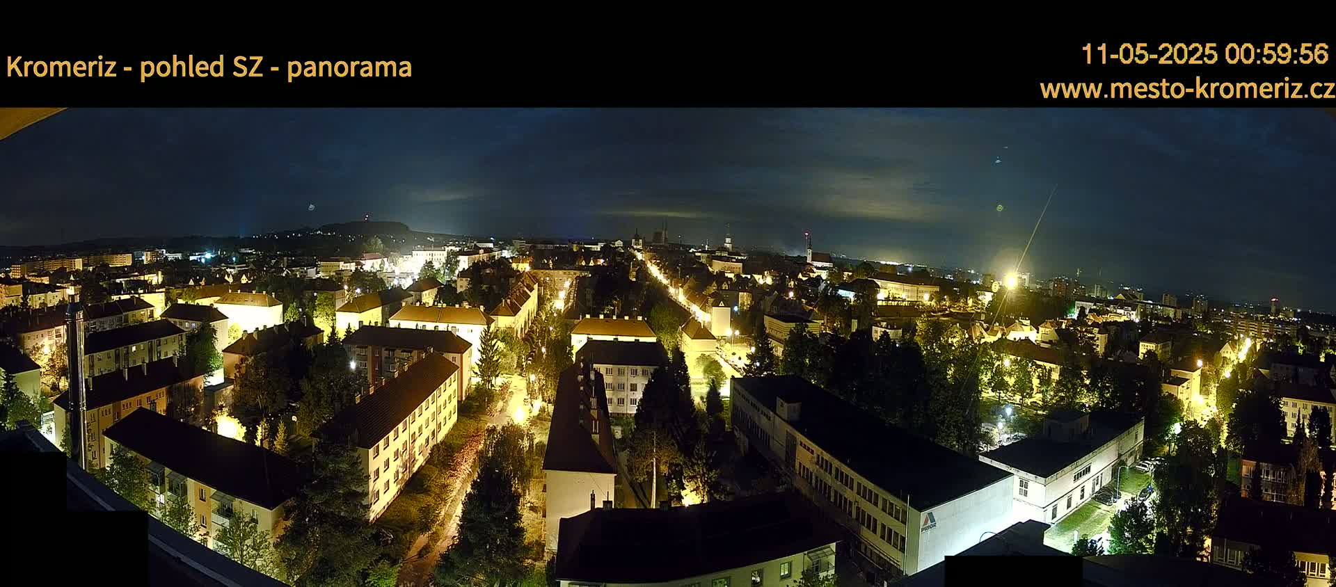 A nighttime panoramic view of a city illuminated by streetlights, under a mostly clear, dark sky.