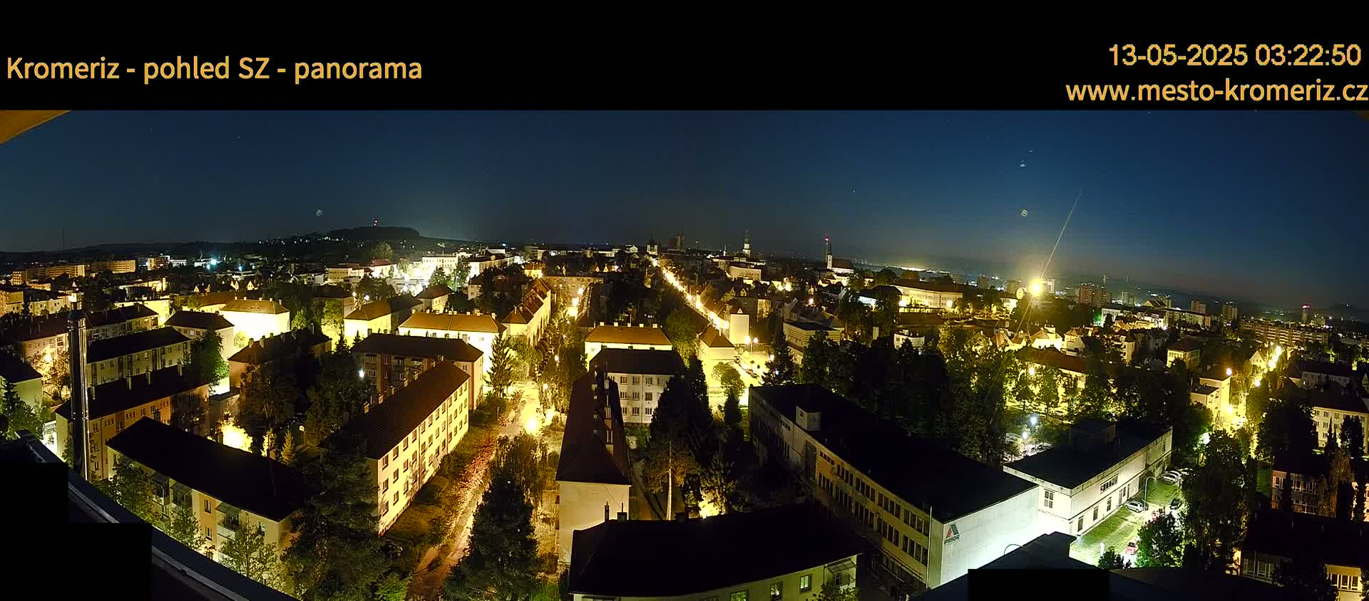 A nighttime panoramic view of a city illuminated by streetlights, under a clear, dark sky.