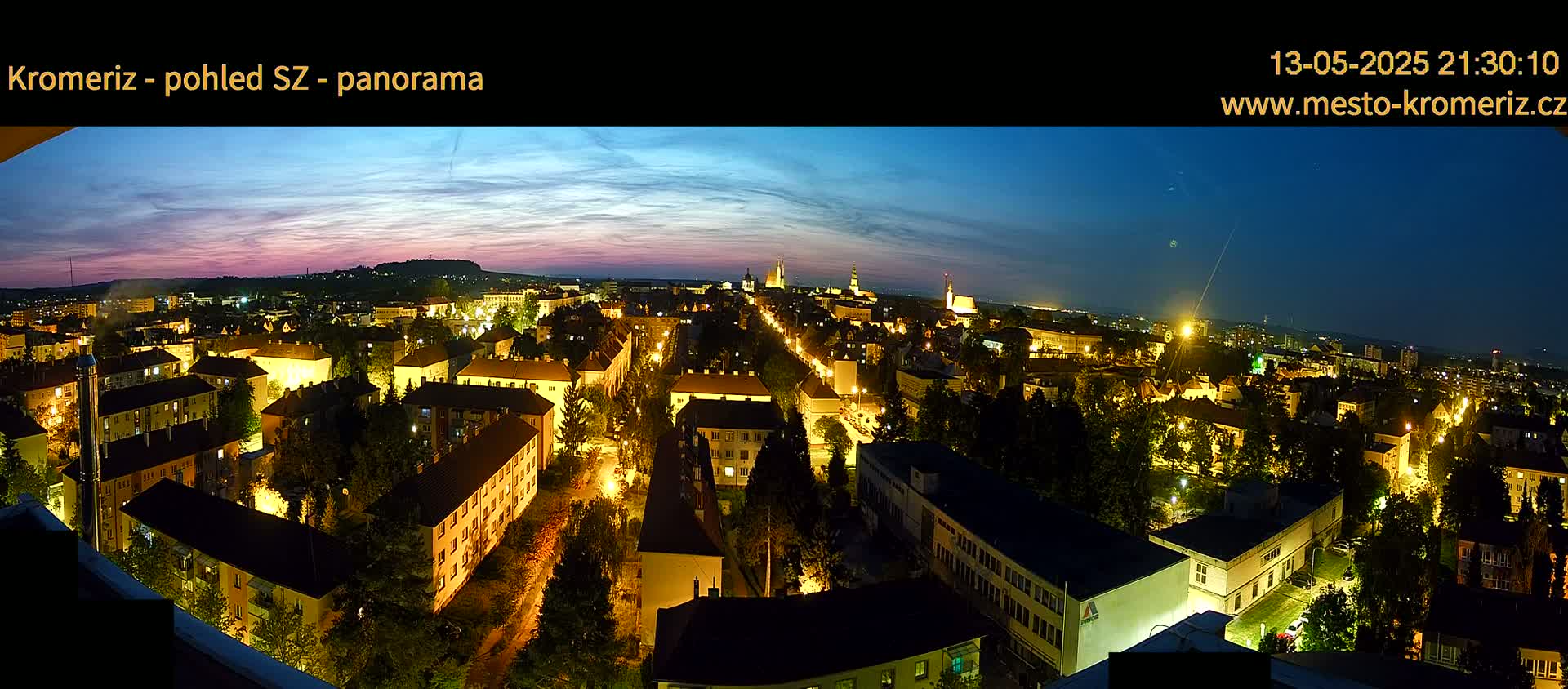 A panoramic night view of a city illuminated by streetlights, under a twilight sky with hints of pink and purple hues.