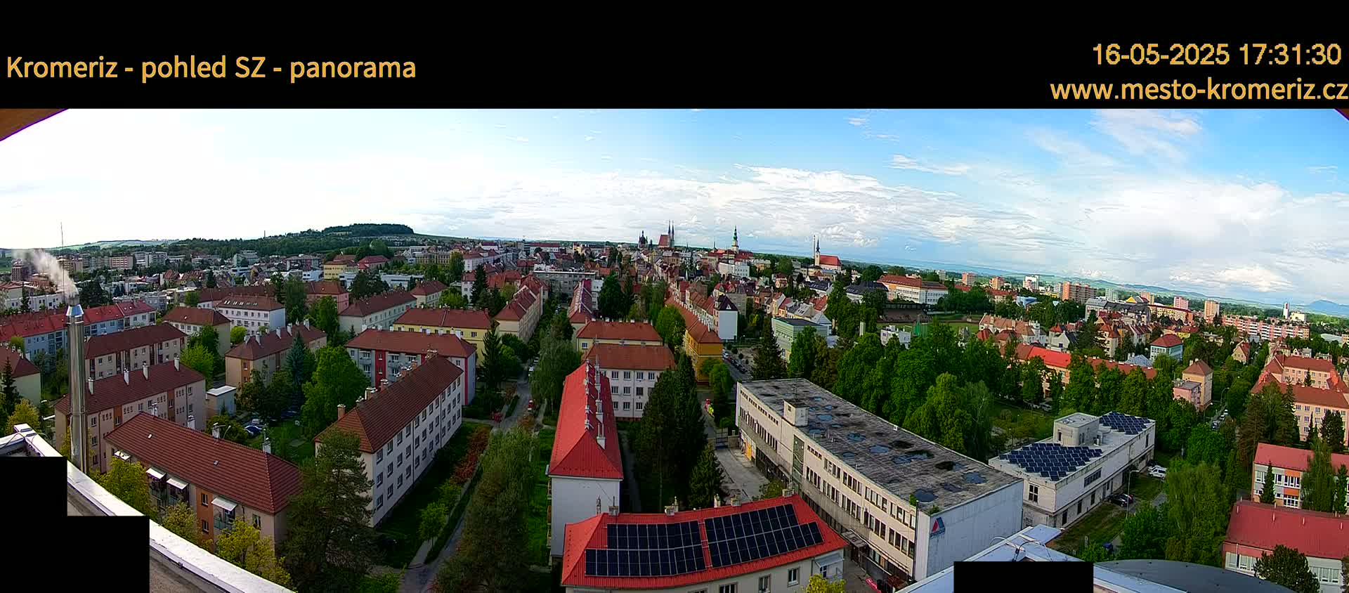 A panoramic view of a town with predominantly red-roofed buildings, under a partly cloudy sky.