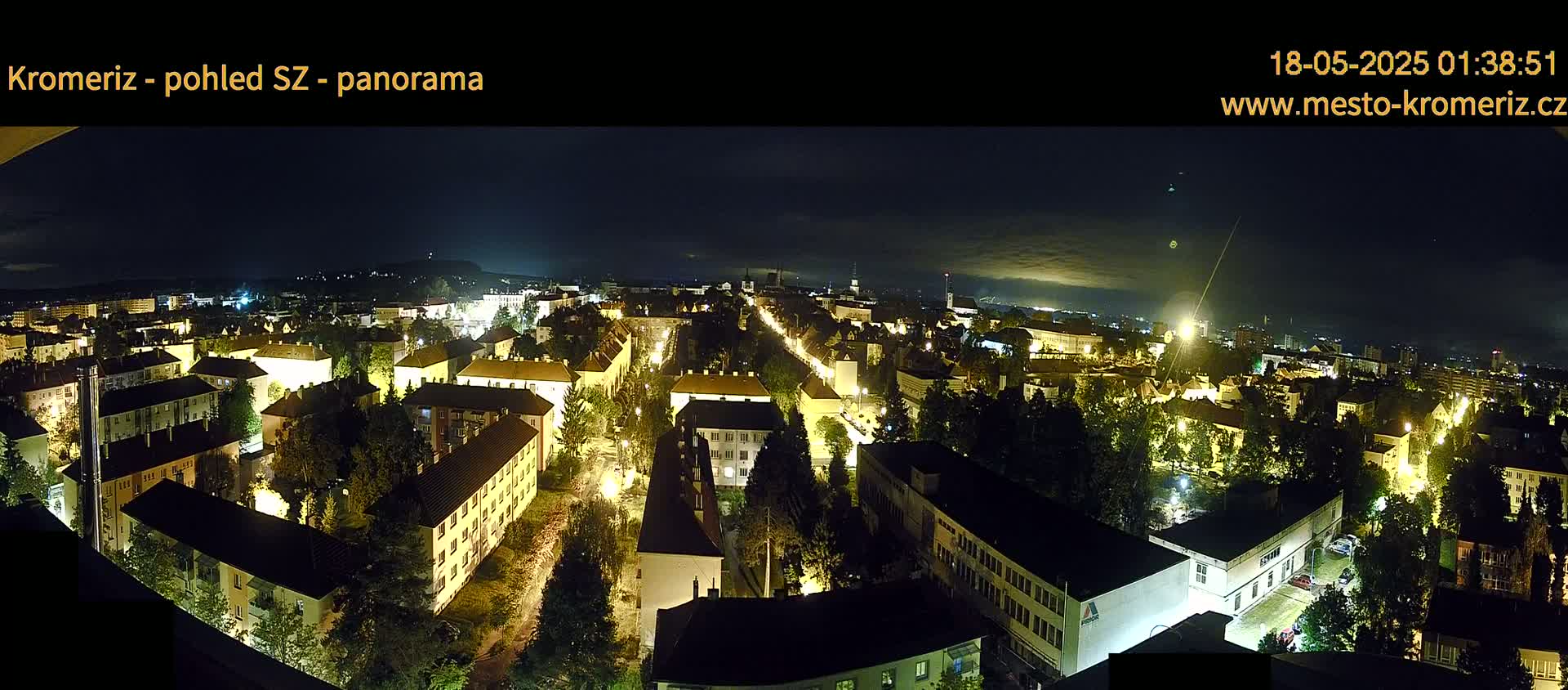 A panoramic nighttime view of a city with illuminated buildings and streets, under a partly cloudy sky.
