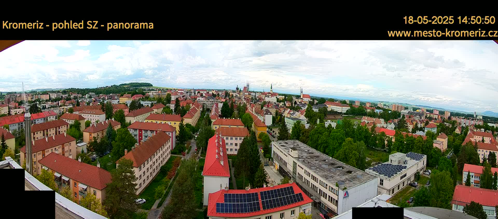 A panoramic view of a town with predominantly red-roofed buildings, under a partly cloudy sky.