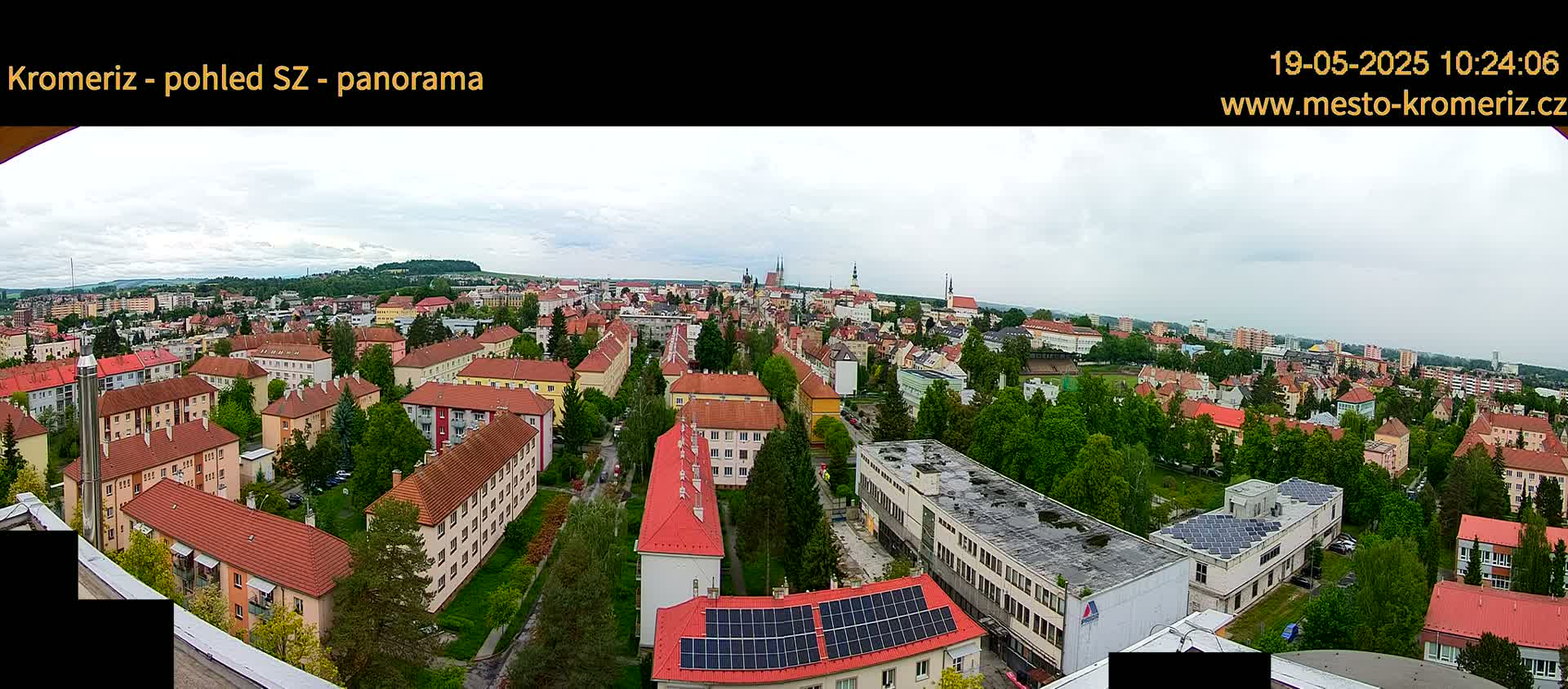 A panoramic view of a city with predominantly red-roofed buildings under a cloudy sky.