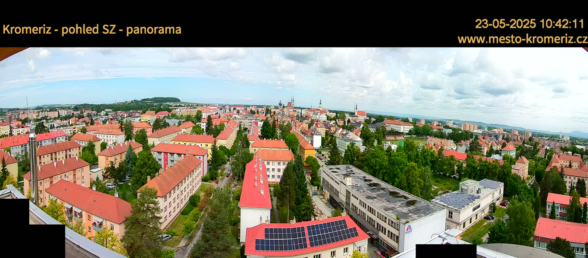 A panoramic view of a town with many red-roofed buildings under a partly cloudy sky.