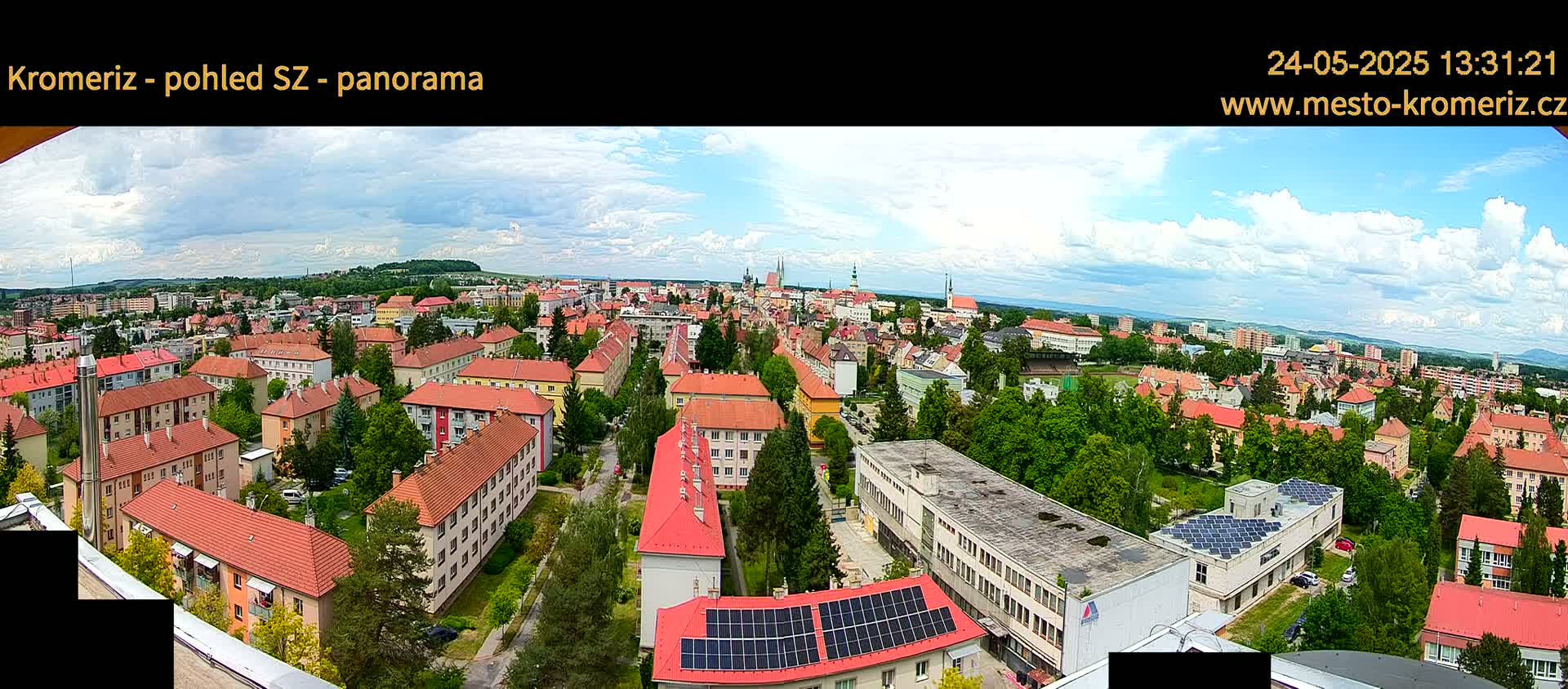 A panoramic view of a town with predominantly red-roofed buildings under a partly cloudy sky.