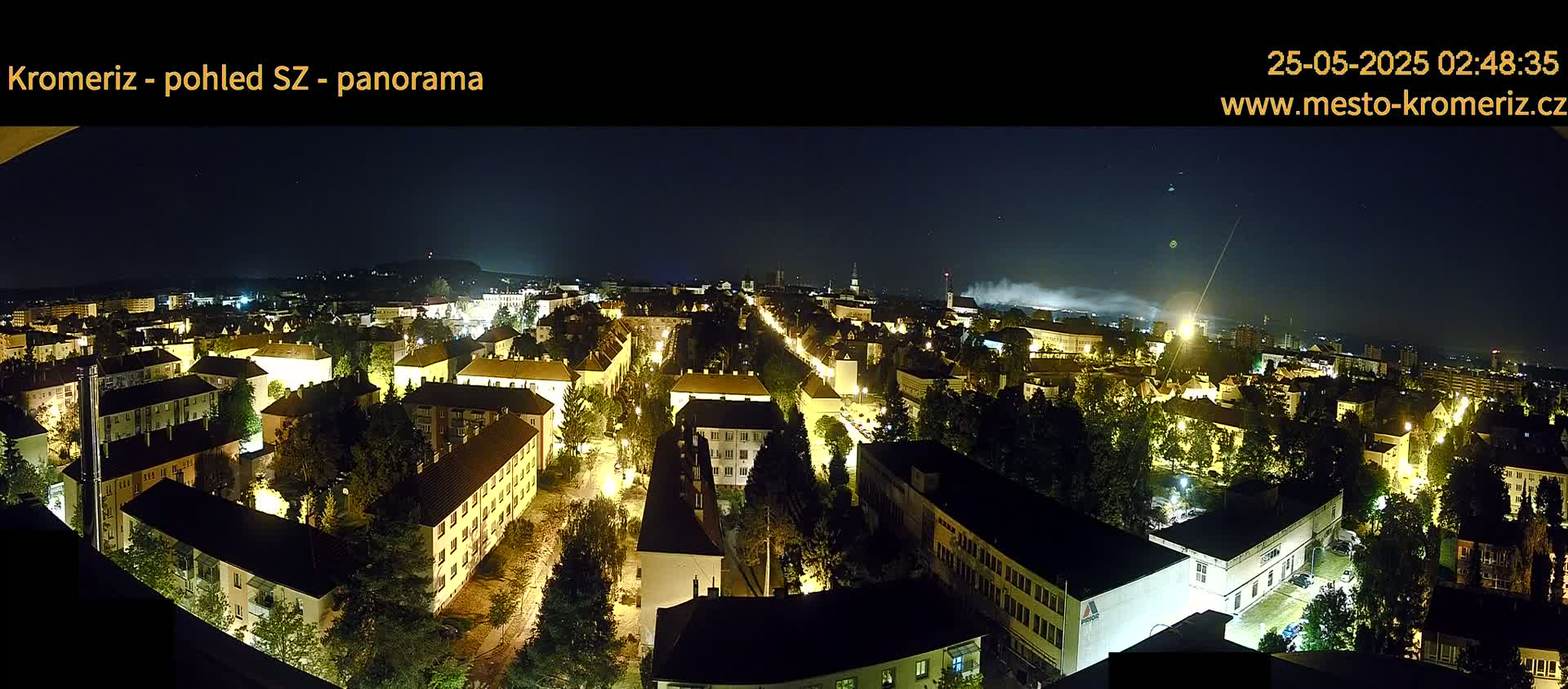 A nighttime panoramic view of a city illuminated by streetlights, with a hazy or smoky atmosphere in the distance under a clear, dark sky.