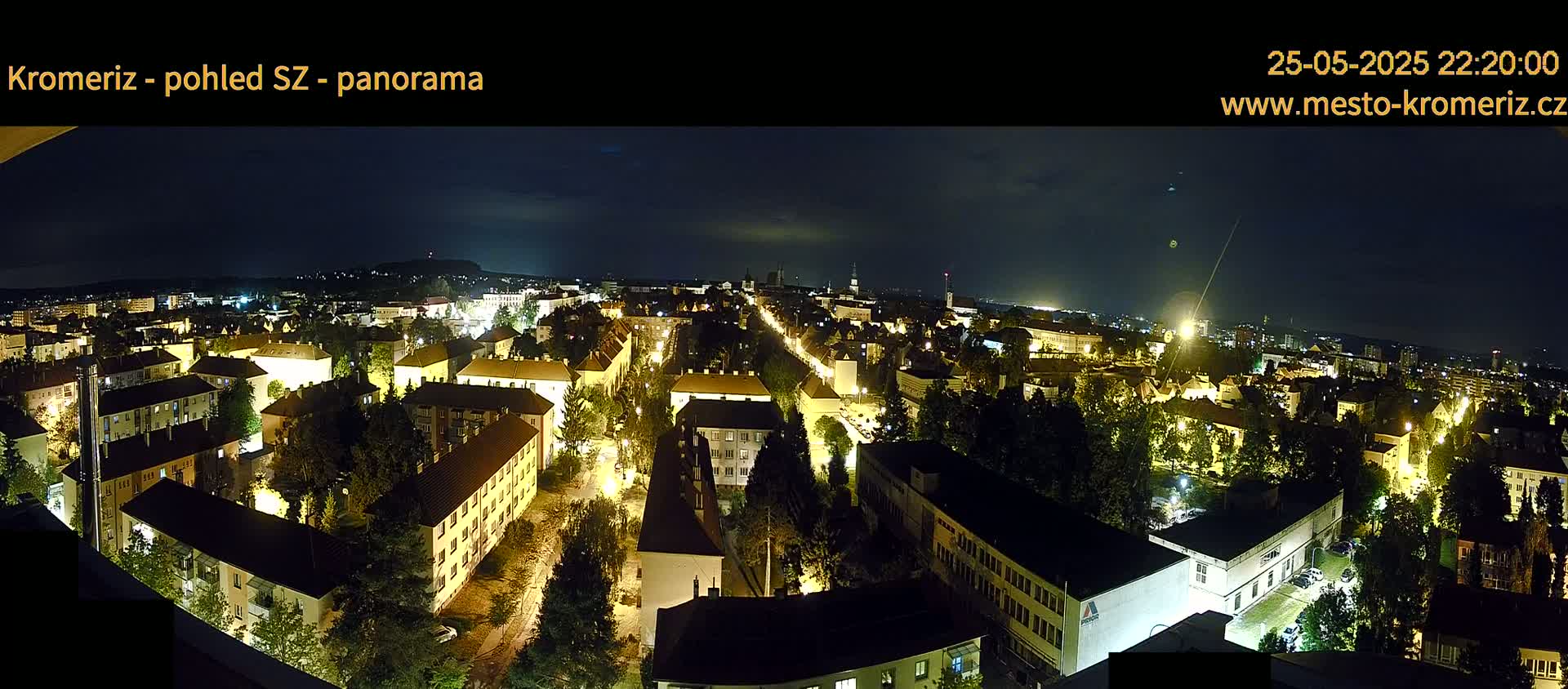 A nighttime panoramic view of a city, illuminated by streetlights and building lights, under a mostly clear dark sky.