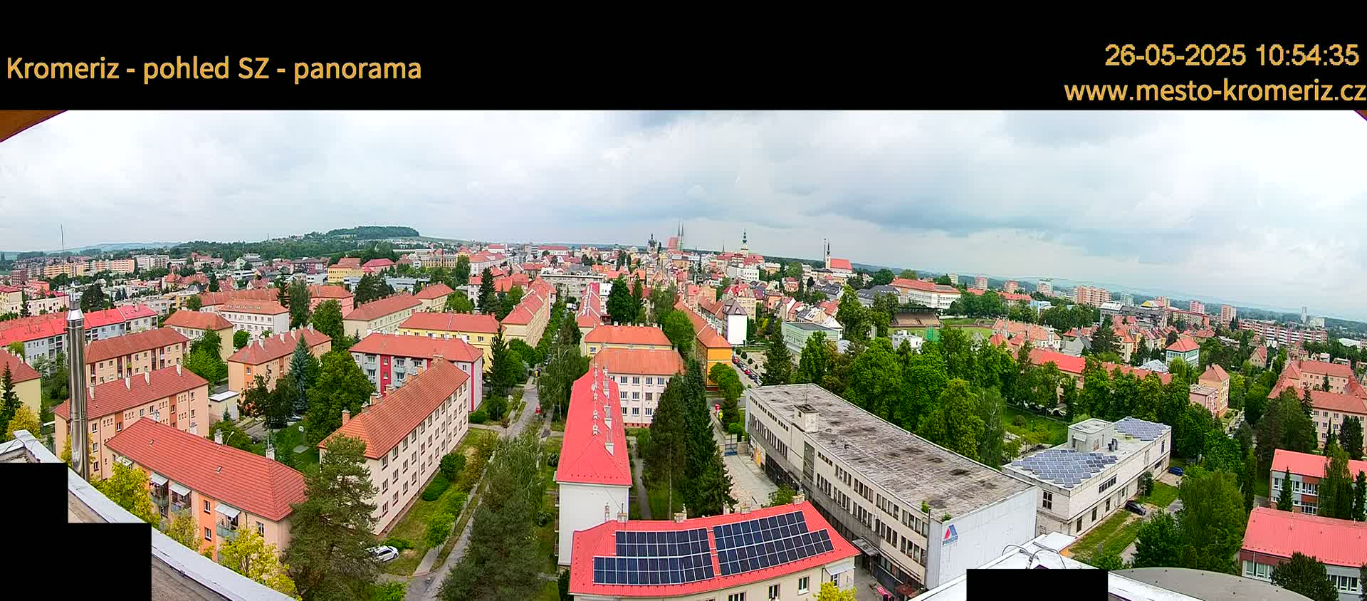 A panoramic view of a town with mostly red-roofed buildings under a partly cloudy sky.