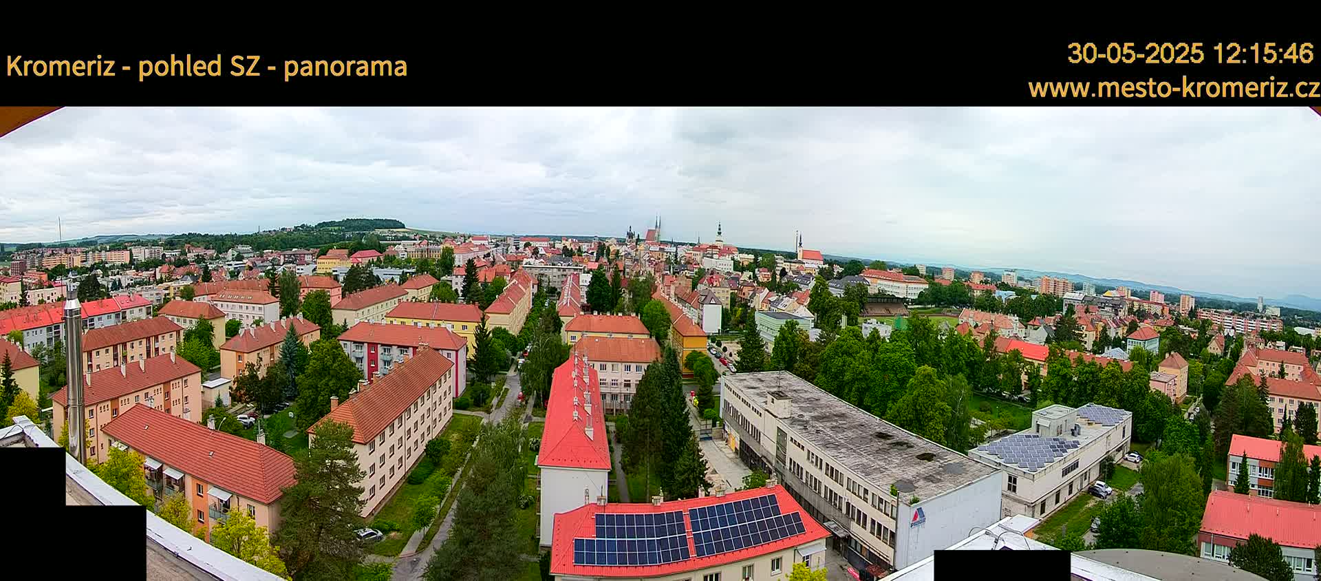 A panoramic view of a town with many red-roofed buildings under a partly cloudy sky.