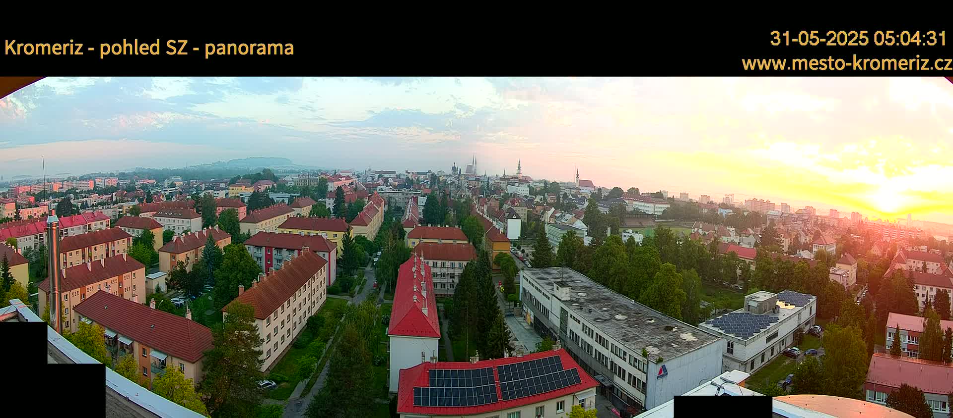 A panoramic view of a city at sunrise, showing numerous buildings and a hazy sky.