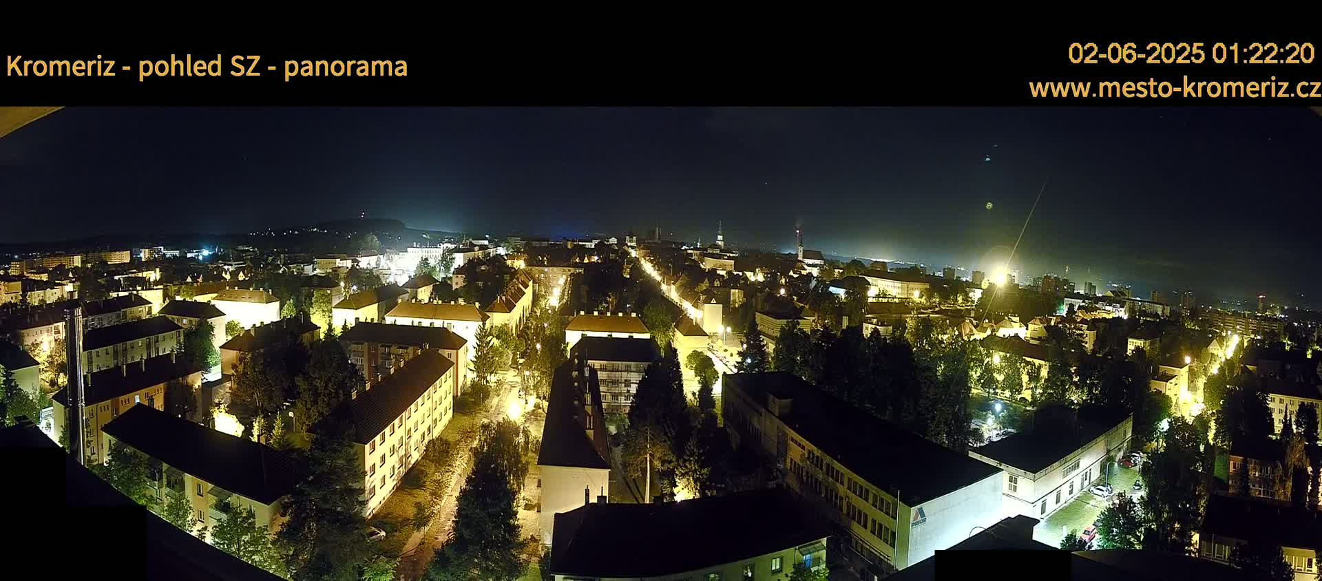 A nighttime panoramic view of a city illuminated by streetlights, under a clear, dark sky.