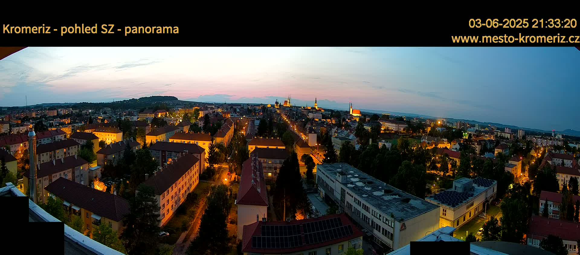A panoramic view of a city at twilight, with buildings illuminated and a soft, dusky sky.