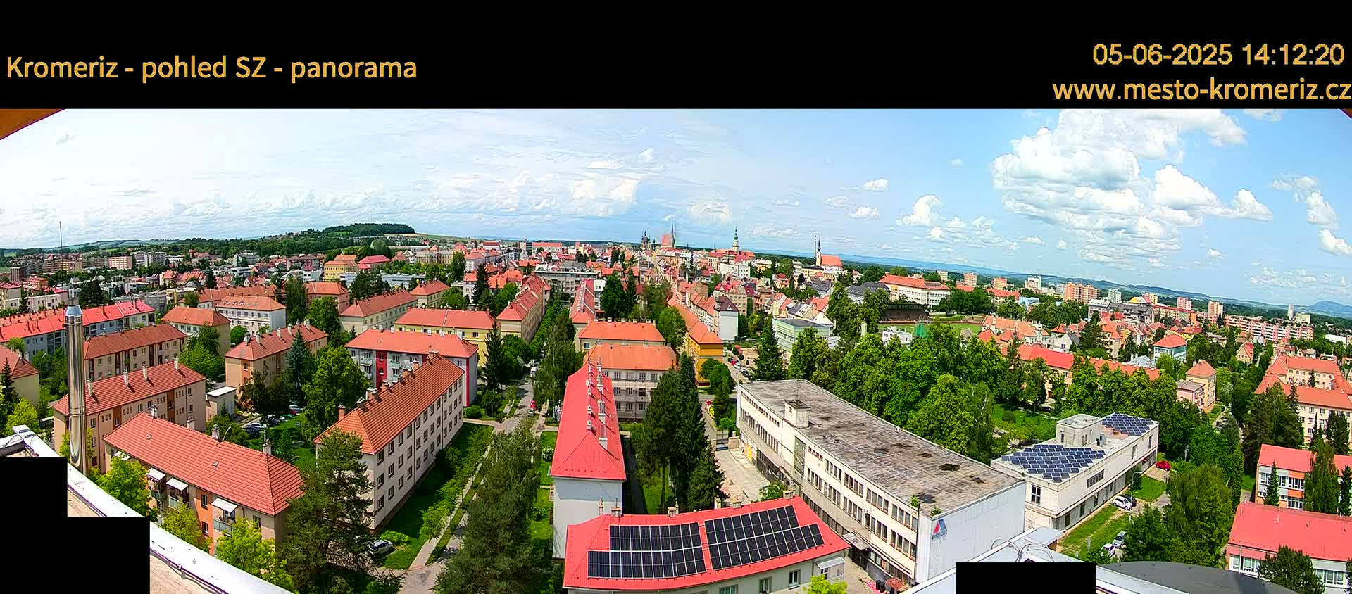 A panoramic view of a town with many red-roofed buildings under a partly cloudy sky.